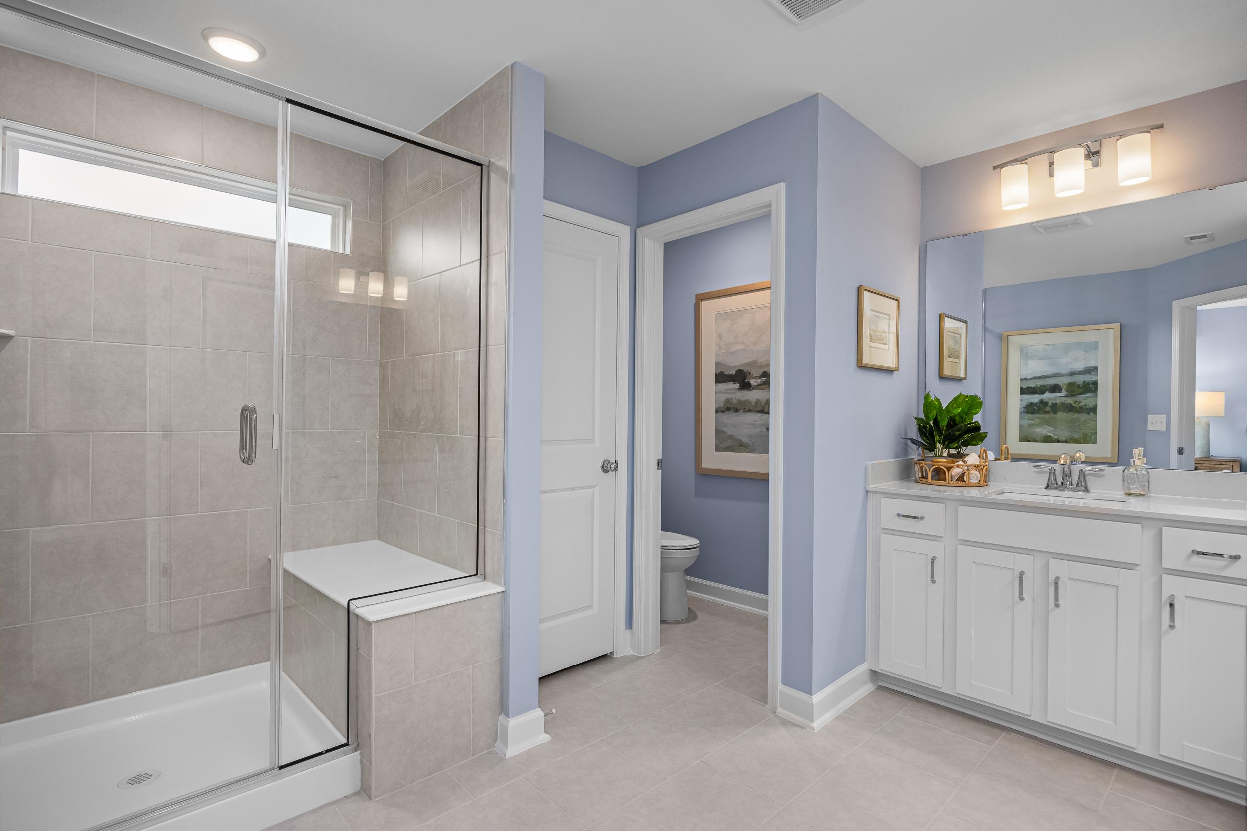 Modern primary bathroom in Springvale, Fuquay-Varina NC with glass walk-in shower, white double vanity, blue walls, and artwork