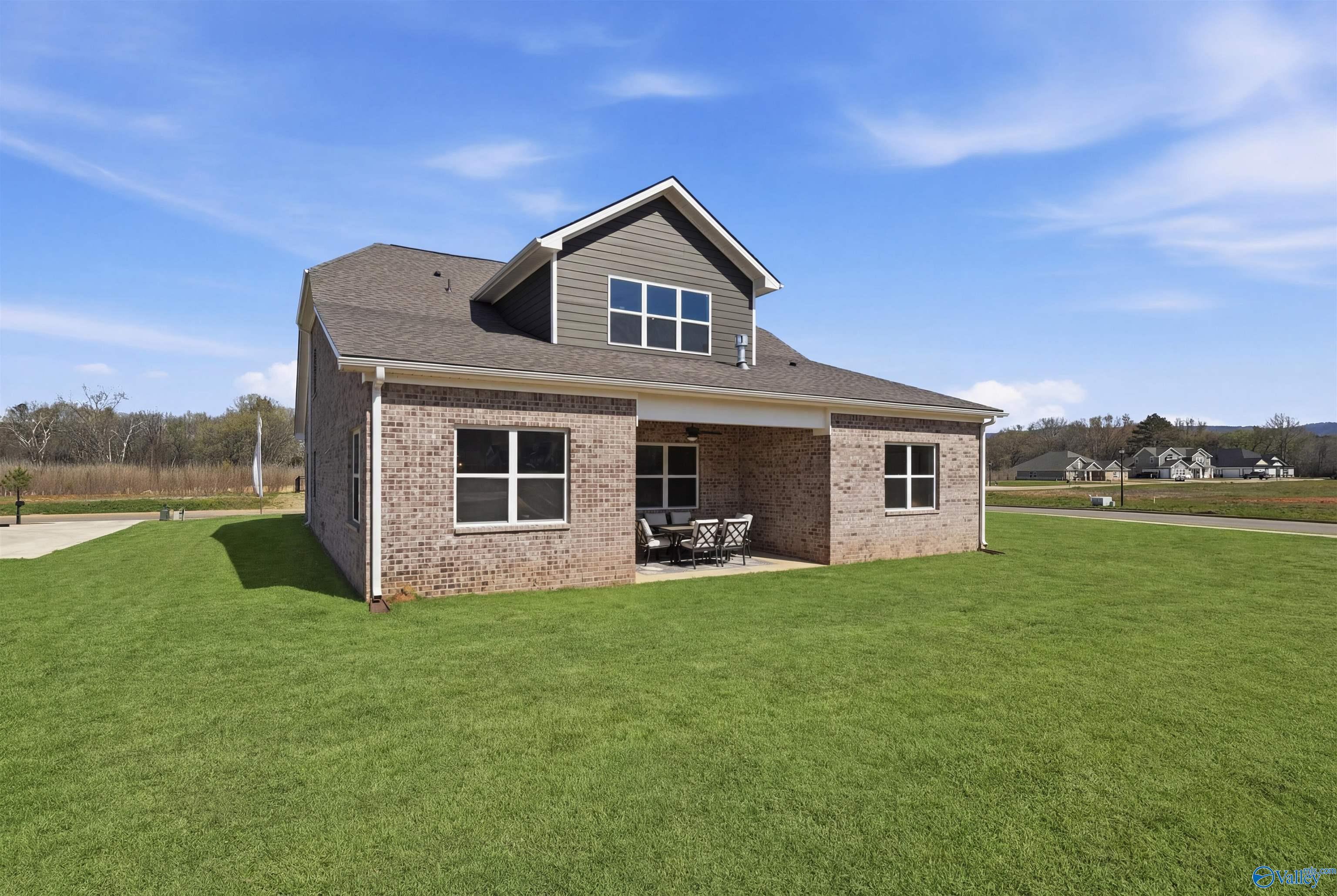 Covered back patio with brick exterior, outdoor seating, and lush green lawn in Evermore Homes Oxford B, Owens Cross Roads, Alabama