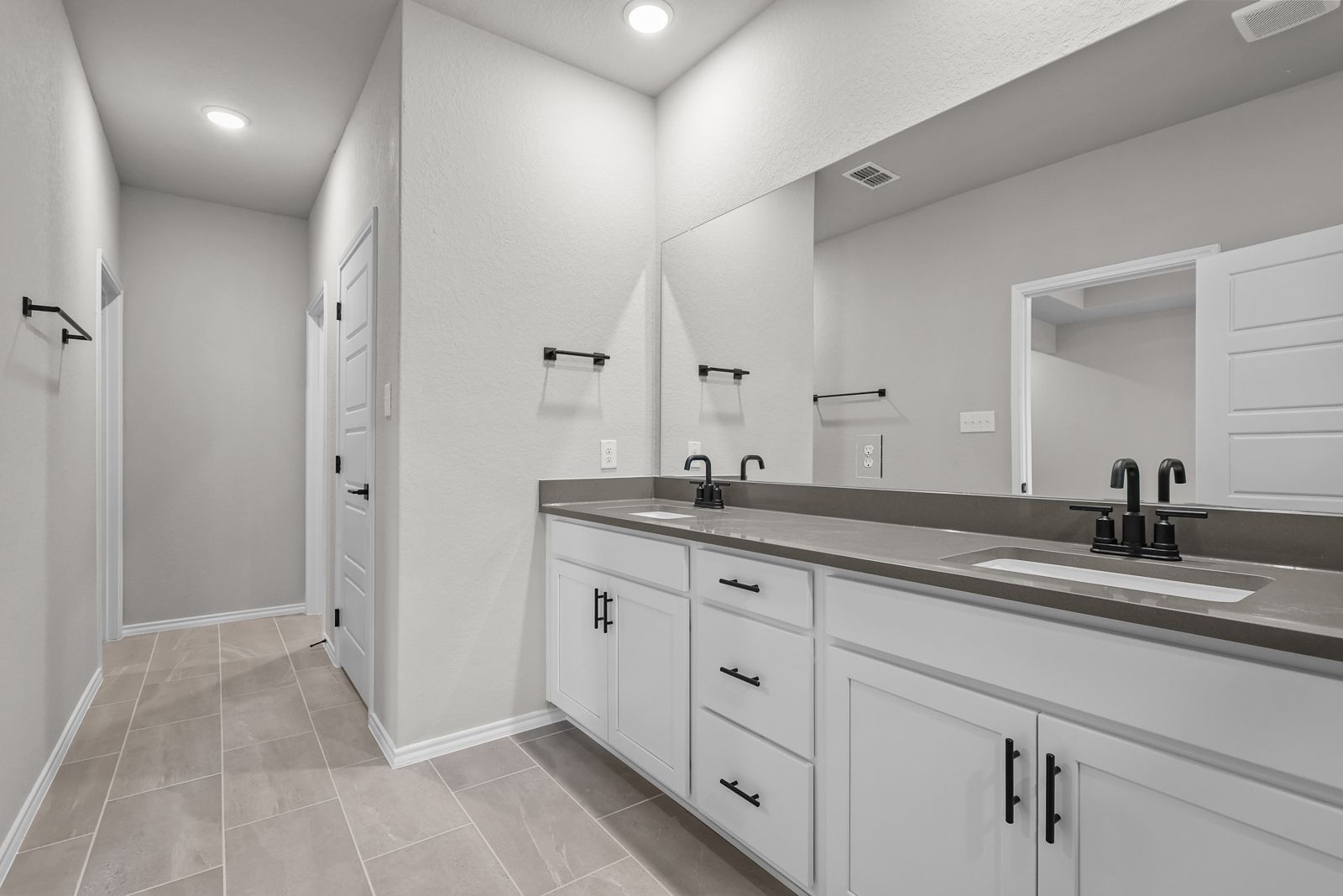 Modern master bathroom in The Glenwood featuring dual vanity with white cabinets, stone countertops, and matte black fixtures.