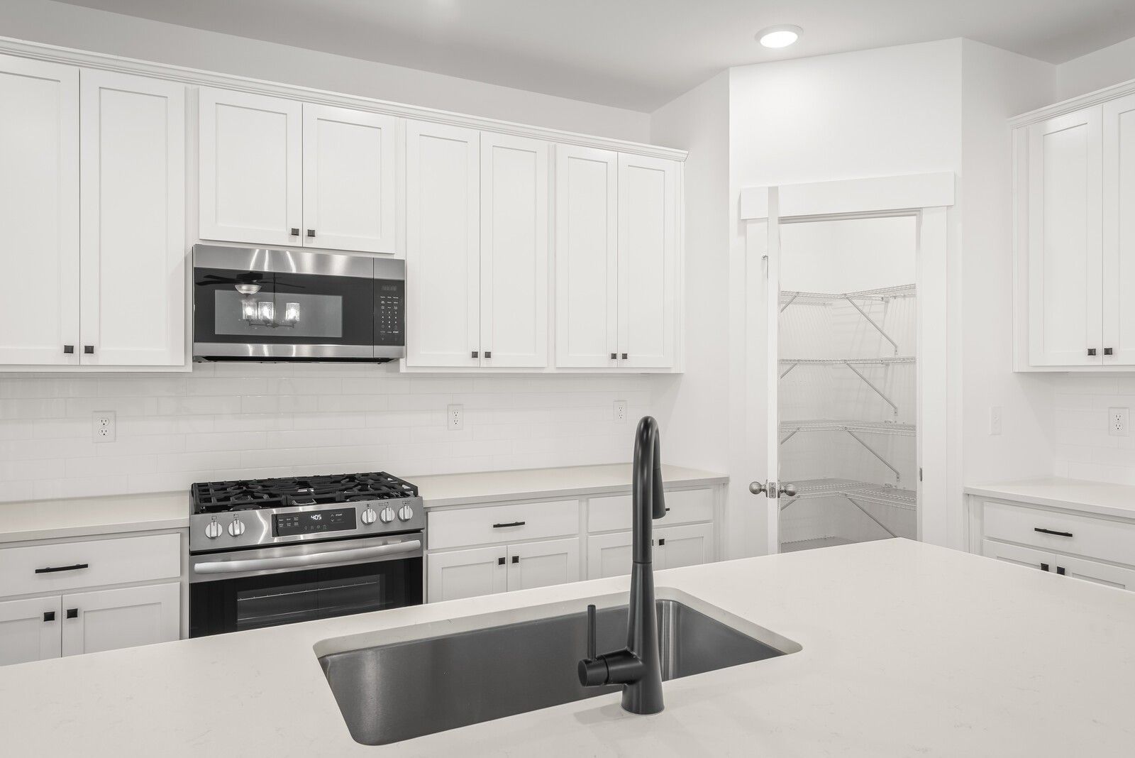 Modern white shaker kitchen with stainless appliances, gas range, and island sink in Davidson Homes The Logan C, Gallatin, TN