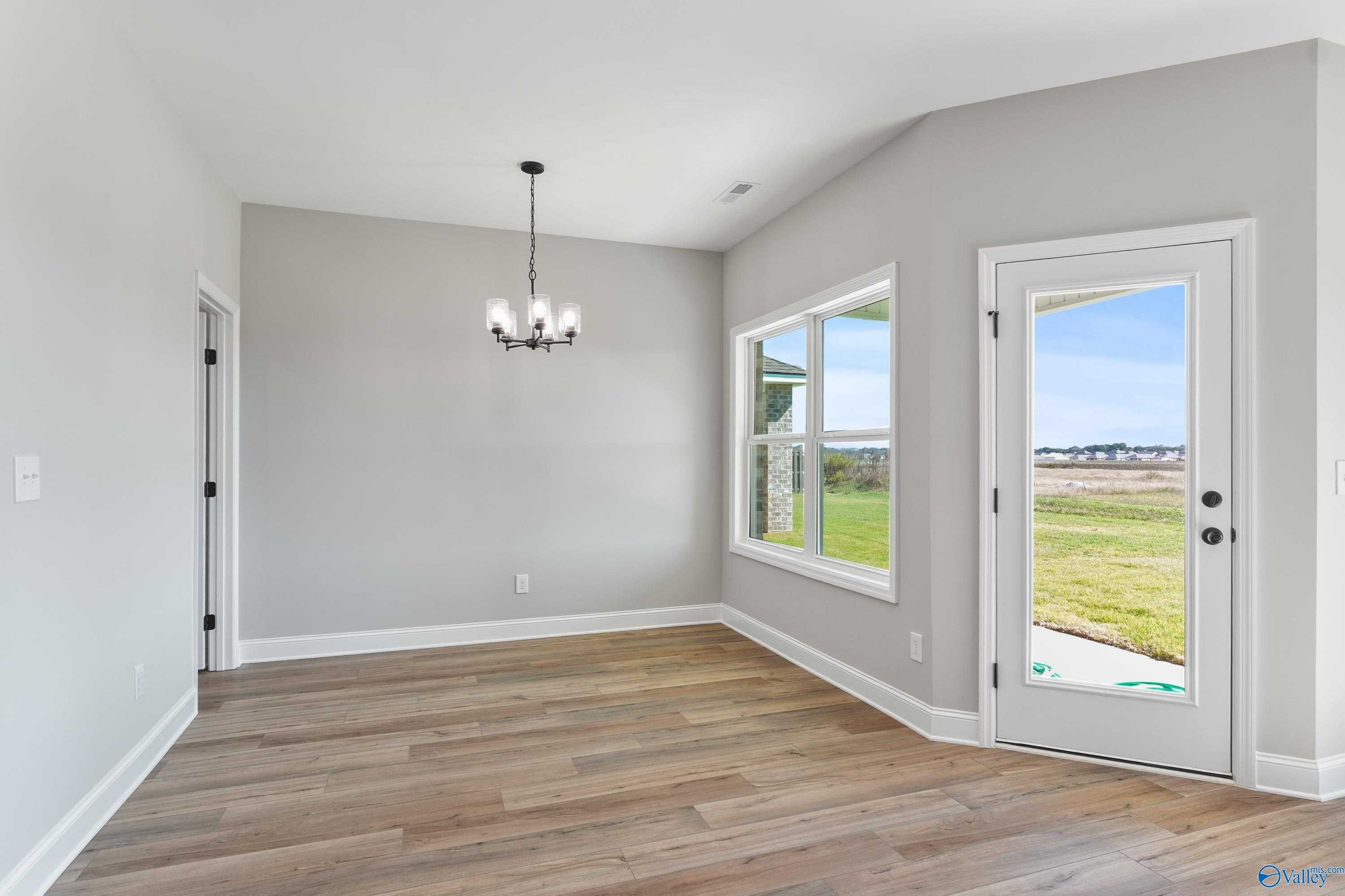 Bright dining room with chandelier, large windows, and glass door to lush backyard in Davidson Homes Daphne C, Hazel Green, Alabama
