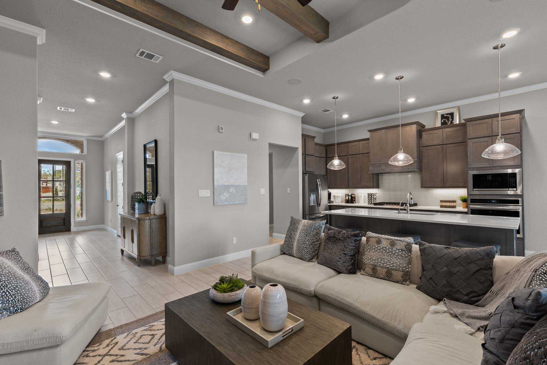 Open-concept living room and kitchen in The Garner A, San Antonio home: gray sectional sofa, quartz island, pendant lights, beamed ceiling