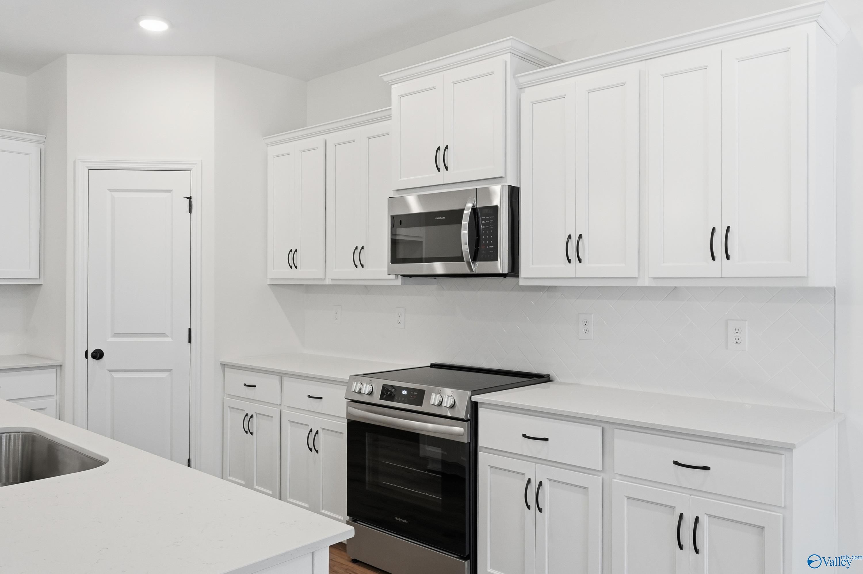 Modern white kitchen featuring stainless steel microwave, oven, and island sink in Davidson Homes The Rockford D, Hazel Green, Alabama