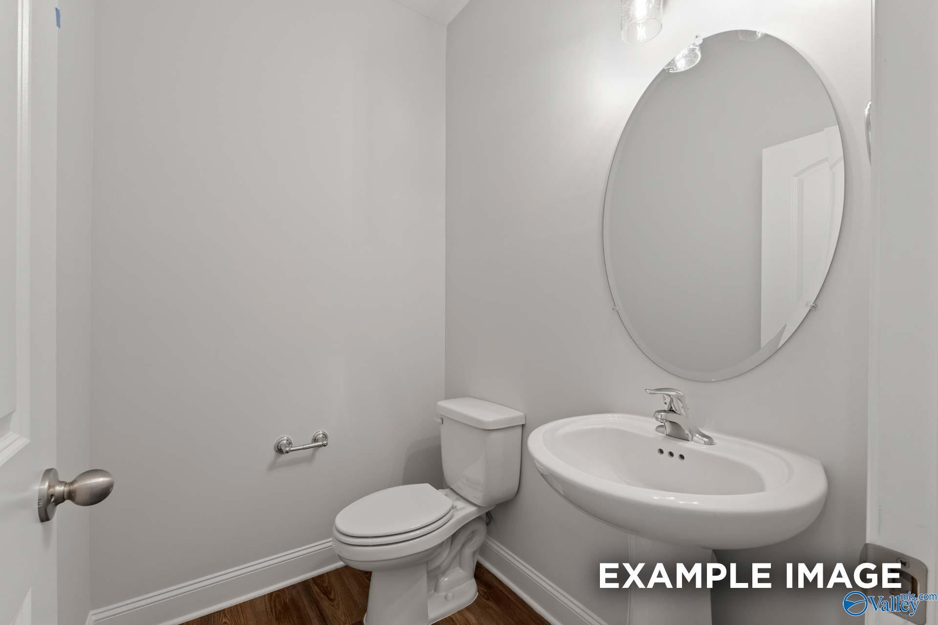 Elegant powder room featuring round mirror, white pedestal sink, and toilet in The Harrison B by Davidson Homes, Decatur, Alabama