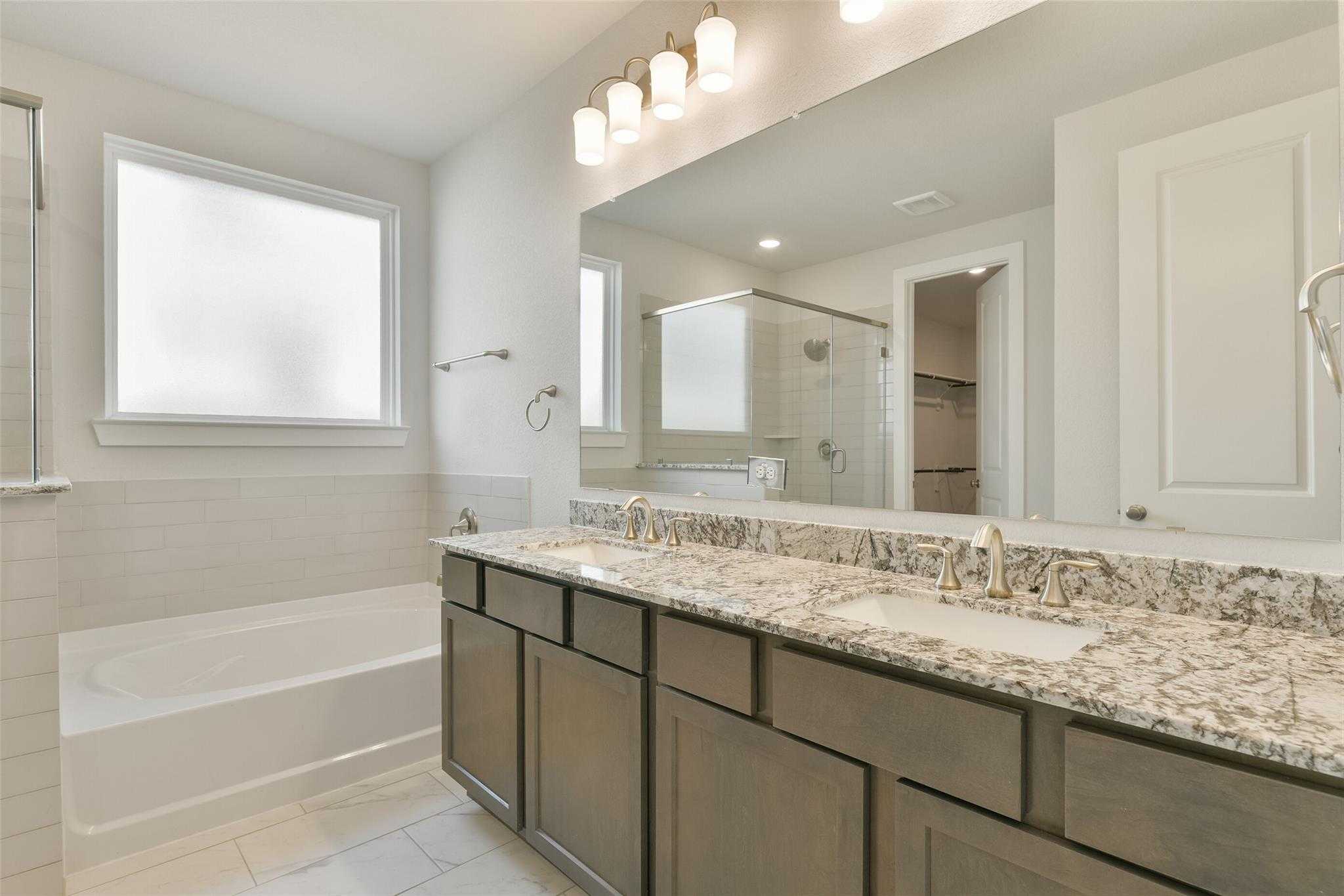 Elegant master bathroom with double quartz vanity, soaking tub, glass shower, and large mirror in Davidson Homes The Edward A, Lago Mar, Texas City