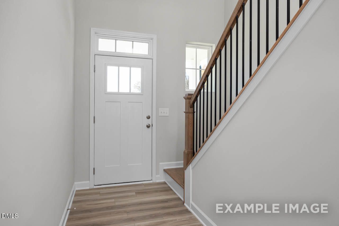 Bright entryway with white paneled door, black metal staircase, and hardwood floors in Davidson Homes The Adalynn A, Lillington, NC