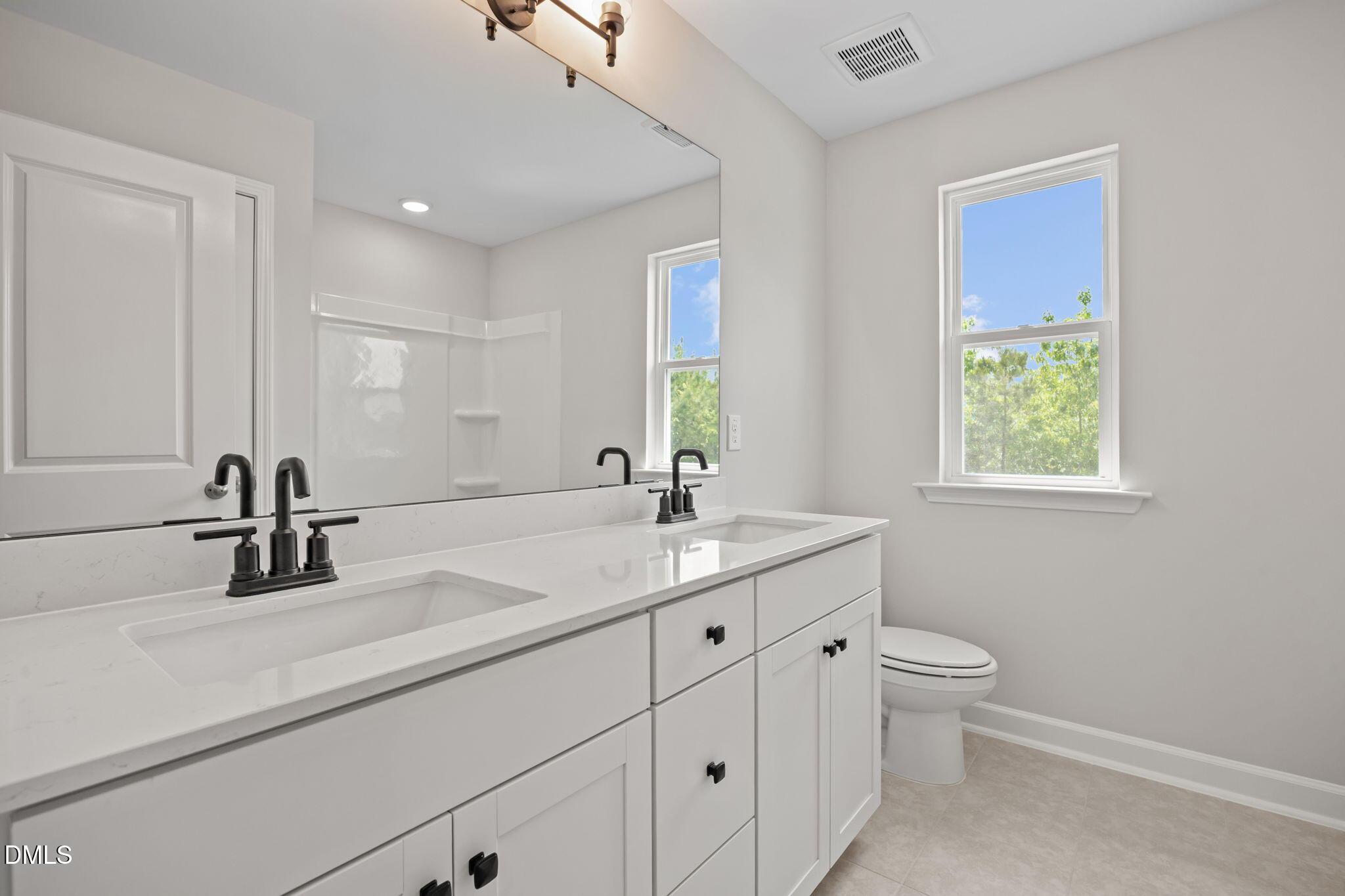 Modern master bathroom double vanity with white quartz counters, black faucets, and window view in Davidson Homes The Willow D, Wendell, NC