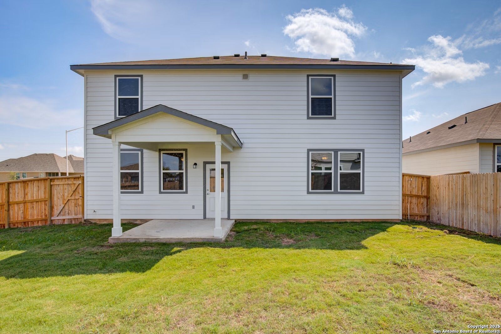 Rear view of two-story white Douglas B home with covered back porch, large windows, and fenced green backyard in Hannah Heights, Seguin, Texas