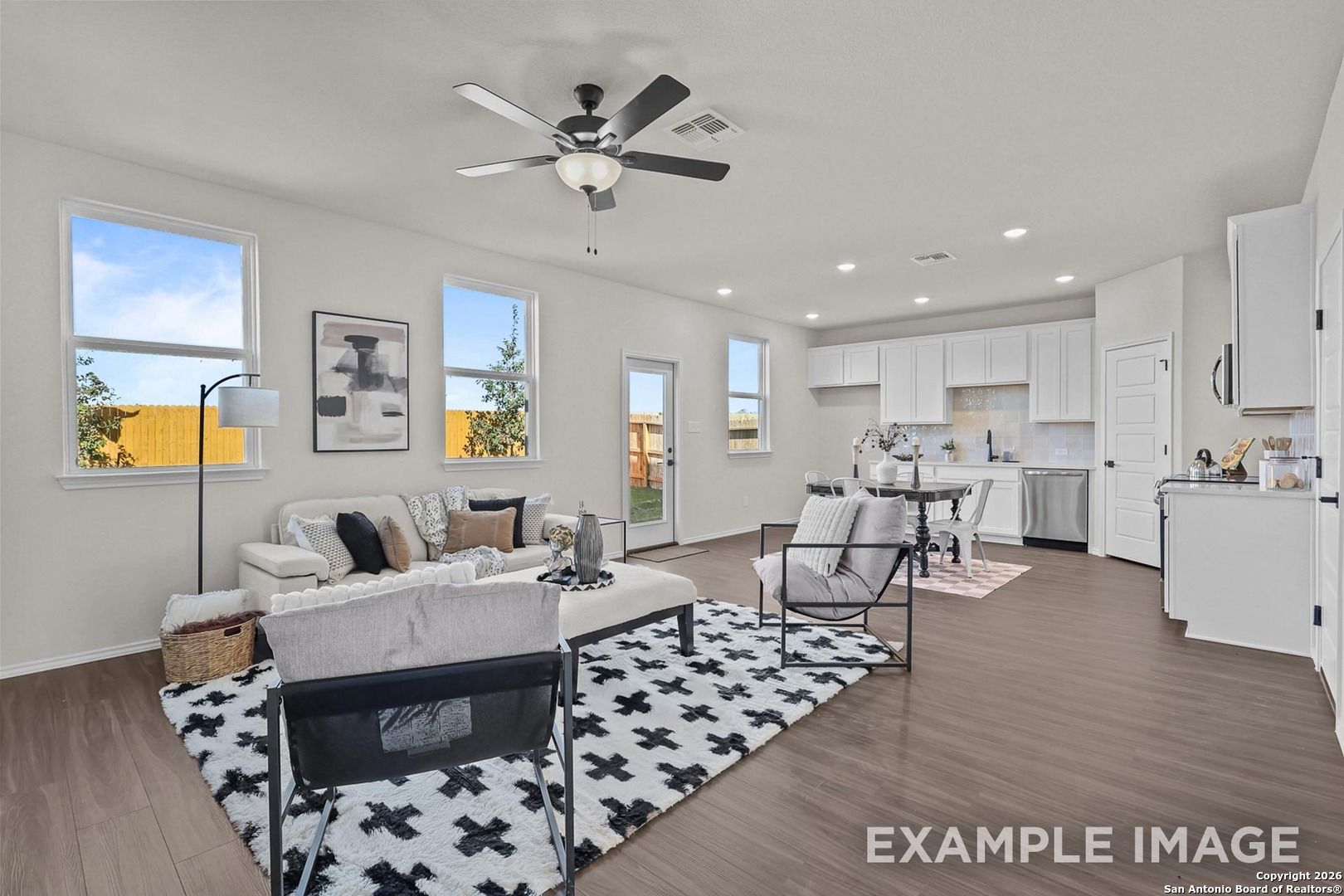 Open-concept living room with white sofa, black rug, ceiling fan, and modern kitchen in Davidson Homes The Trinity B, San Antonio