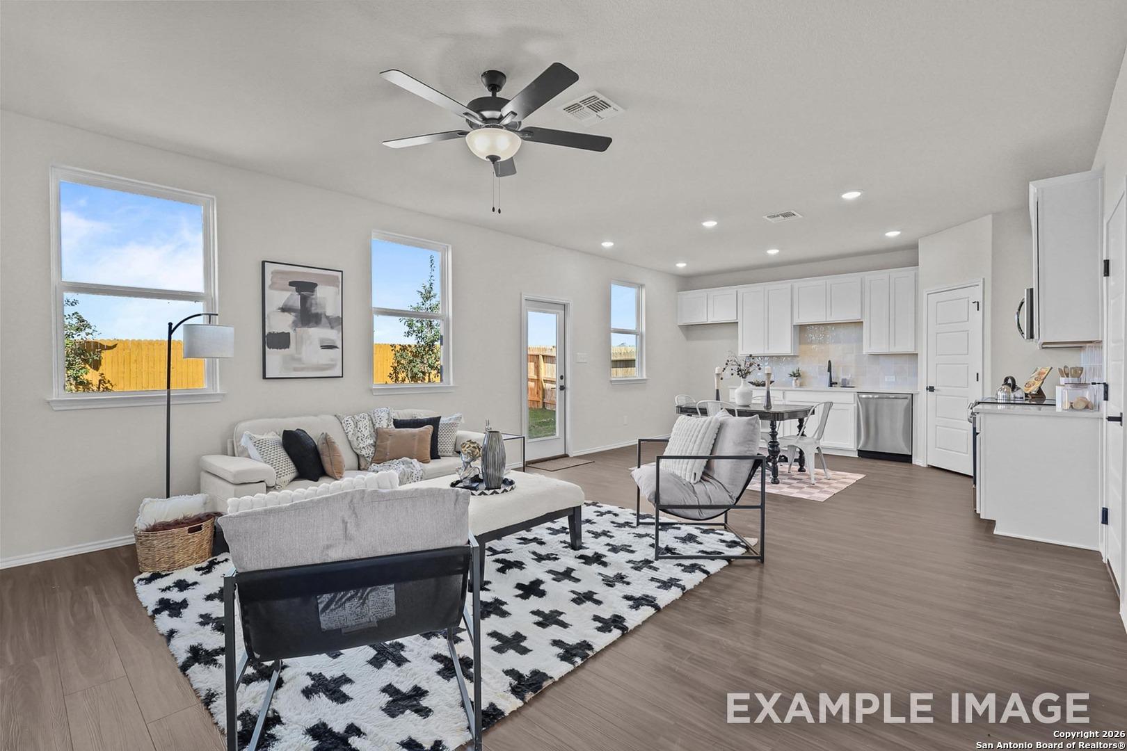 Open-concept living room with white sofa, black rug, ceiling fan, and modern kitchen in Davidson Homes The Trinity B, San Antonio