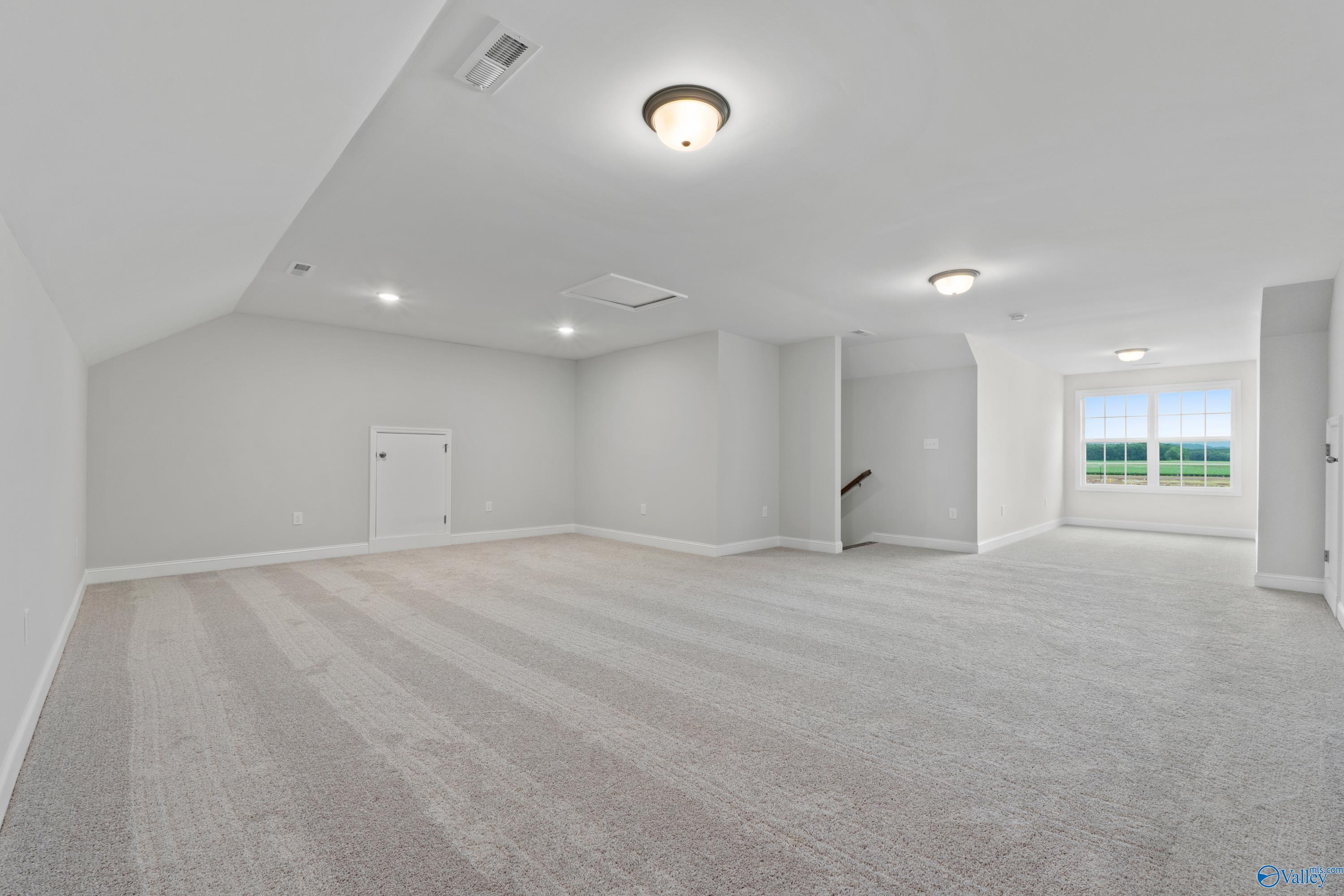 Spacious bonus room with sloped ceiling, beige carpet, and large windows overlooking fields in Davidson Homes Rockford B, Toney, AL