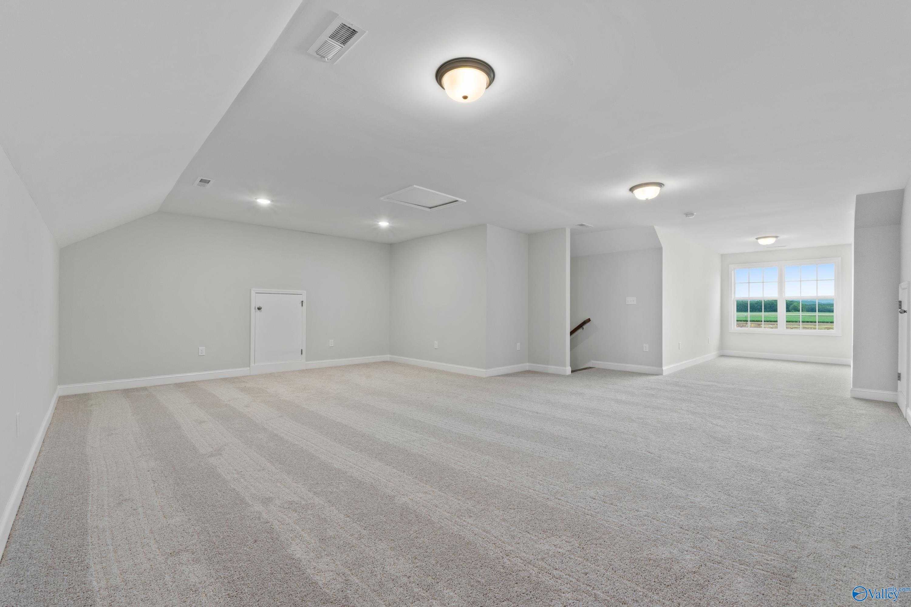 Spacious bonus room with sloped ceiling, beige carpet, and large windows to green field in Davidson Homes The Rockford B, Toney, Alabama
