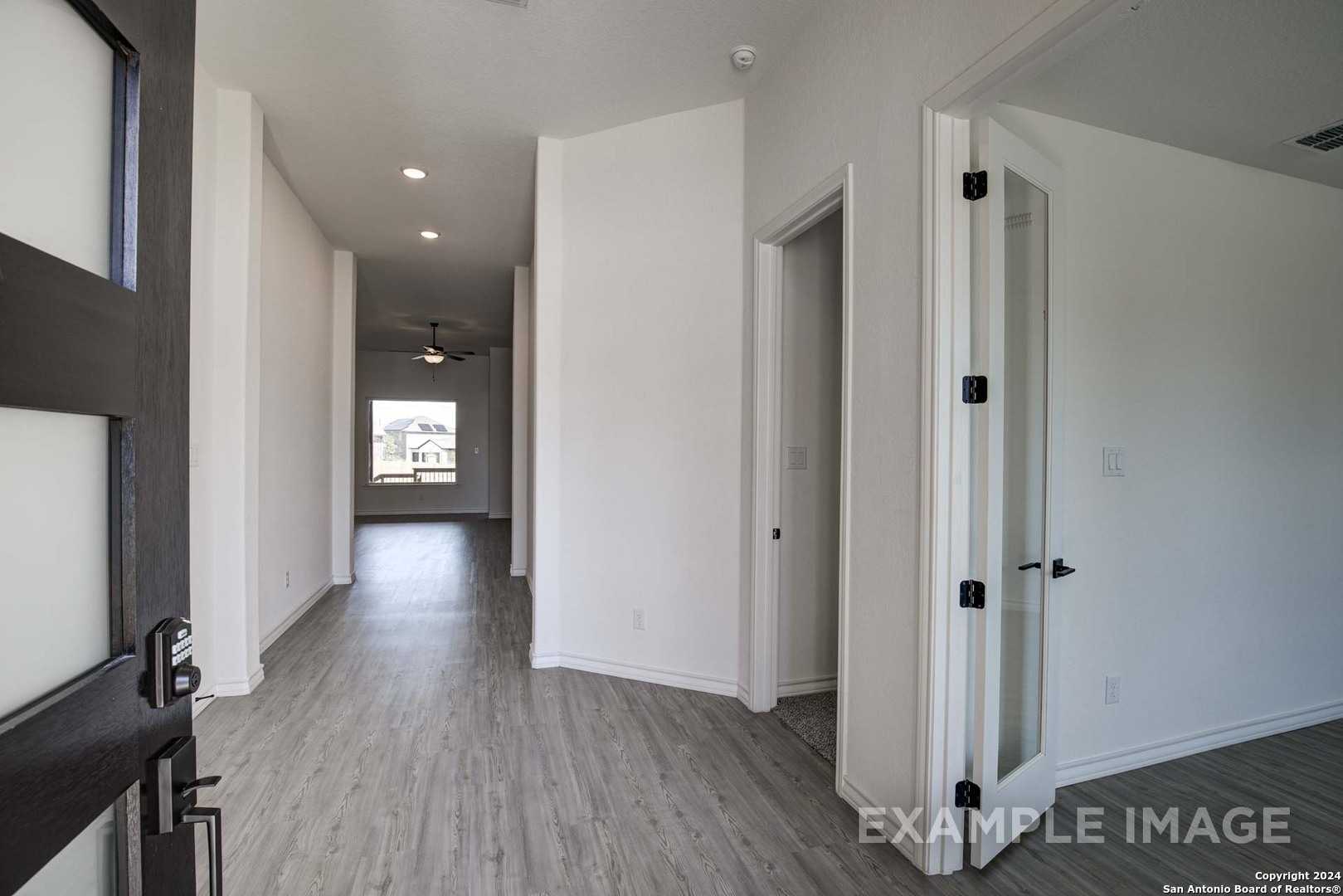 Modern entry hallway with gray luxury vinyl plank flooring, white walls, black front door, and open bedroom doors in Davidson Homes The Garner C, Castroville, Texas