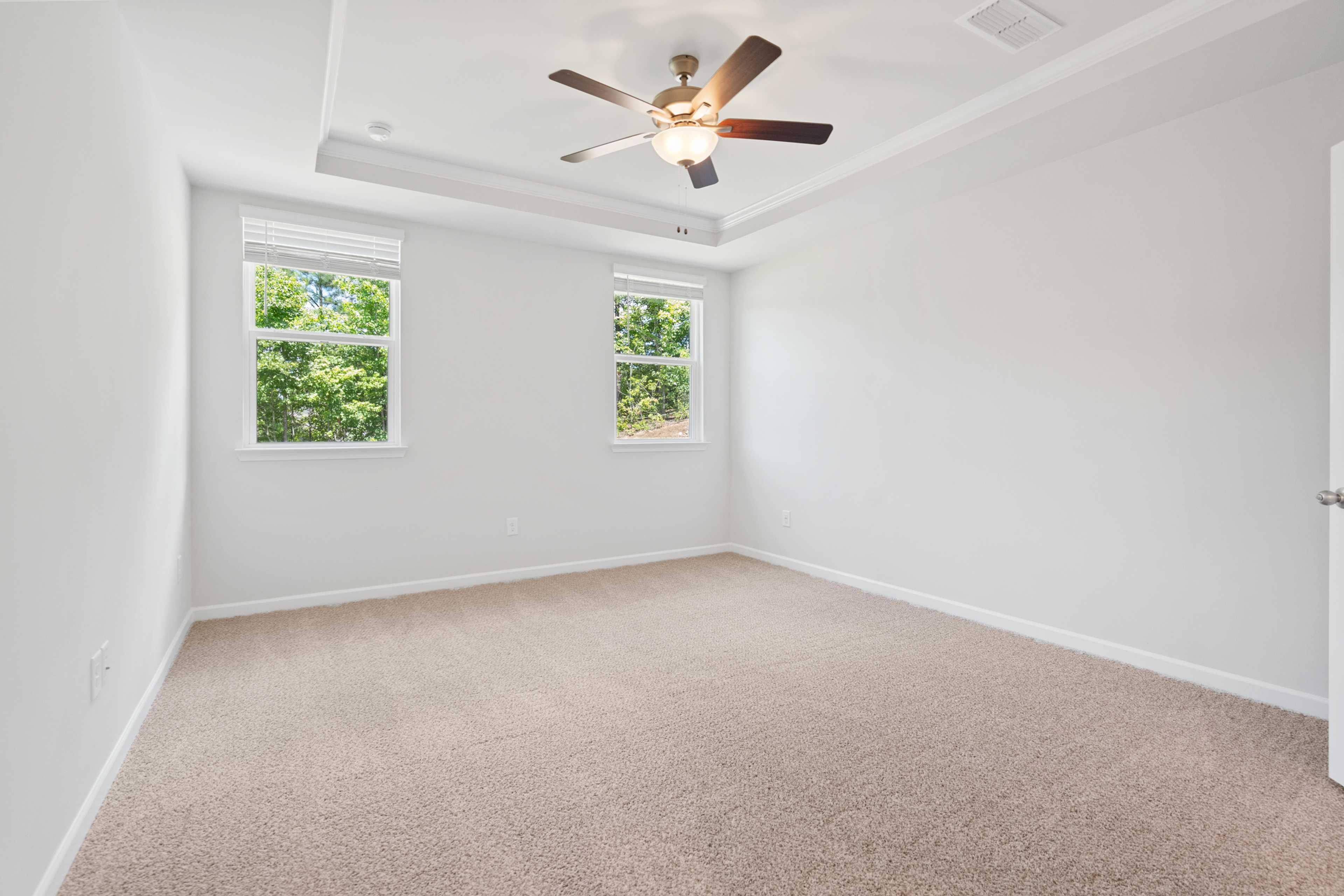Spacious bedroom at Mountainbrook in Cartersville GA by Davidson Homes with white walls, carpet floor, ceiling fan, and large windows