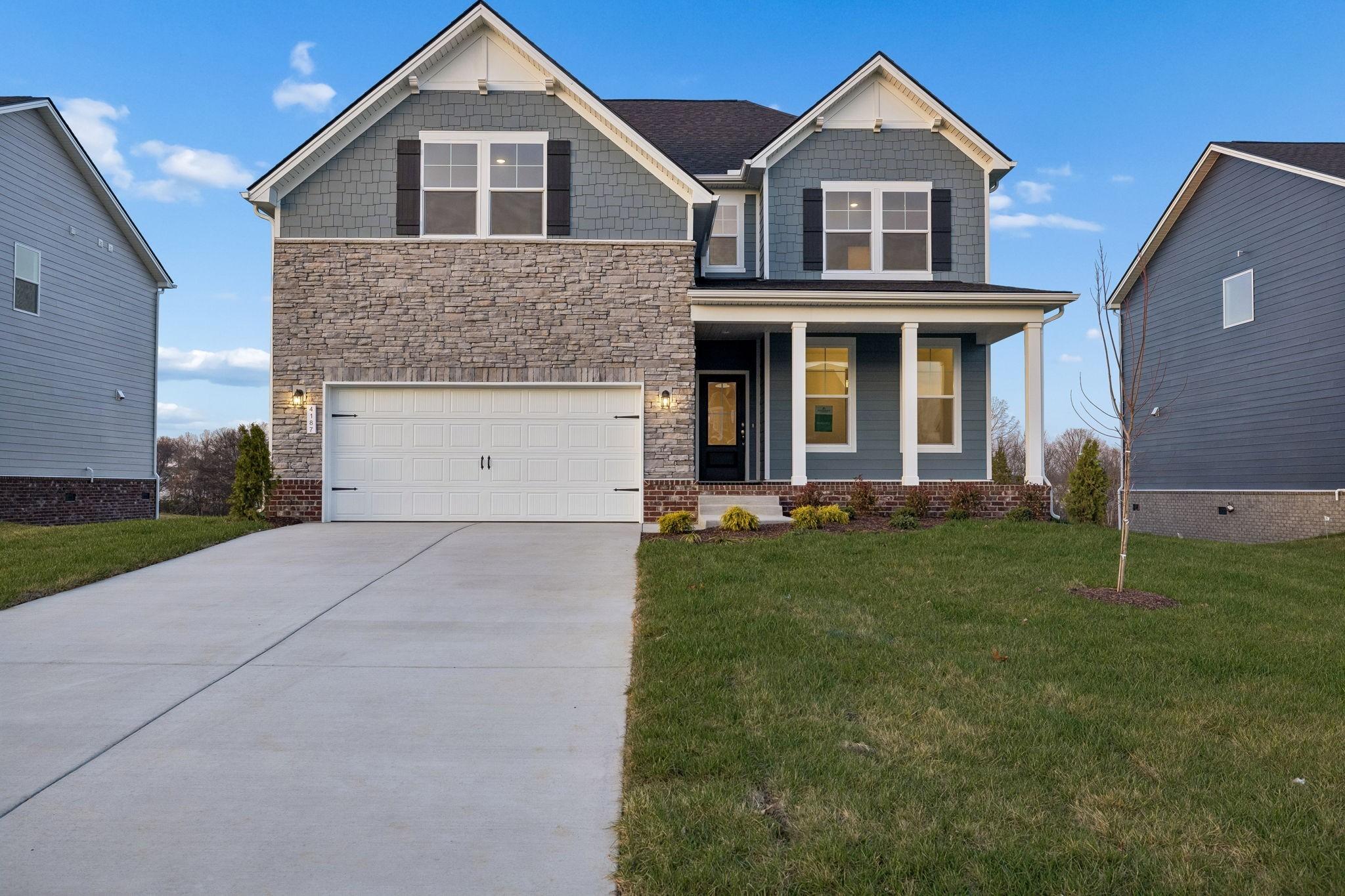Two-story gray Craftsman home with stone accents, covered porch, two-car garage, and landscaped yard in Calista Farms, White House, TN