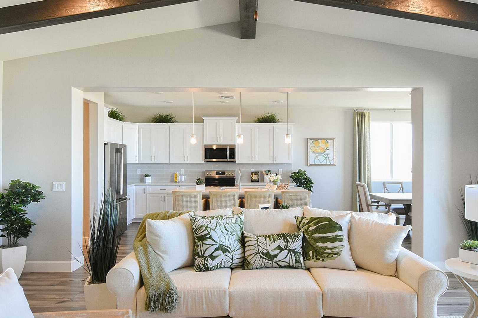 Open-concept living room and kitchen in The Summit B by Evermore Homes, with white sofa, green accents, stainless appliances, and dining nook