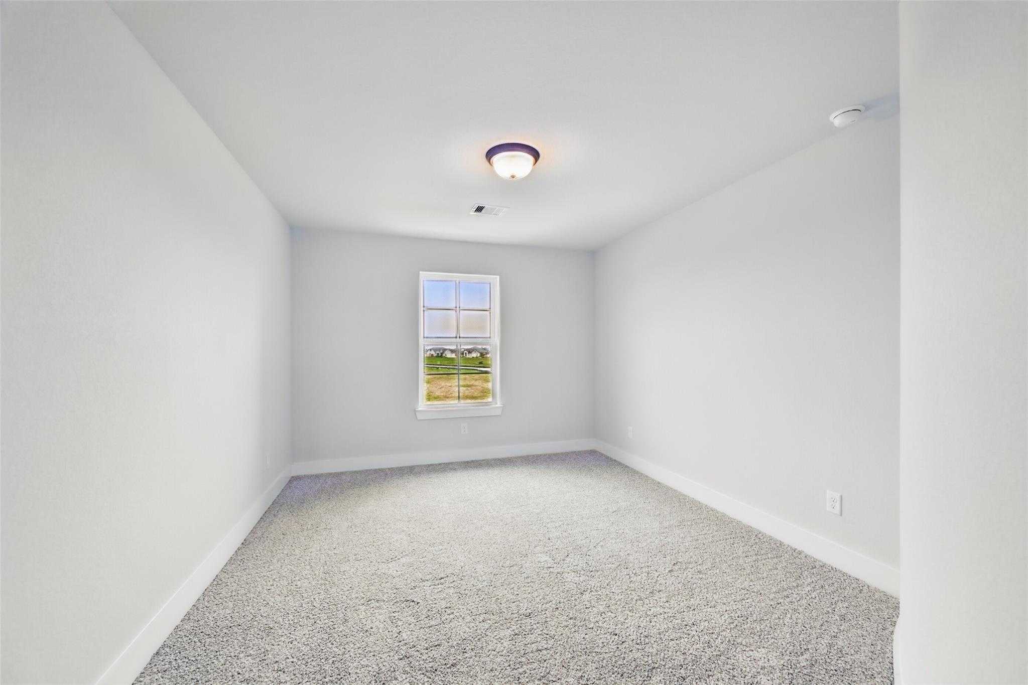 Bright empty bedroom with large window, gray carpet, and light walls in The Victoria C floor plan, Davidson Homes, Lago Mar, Texas
