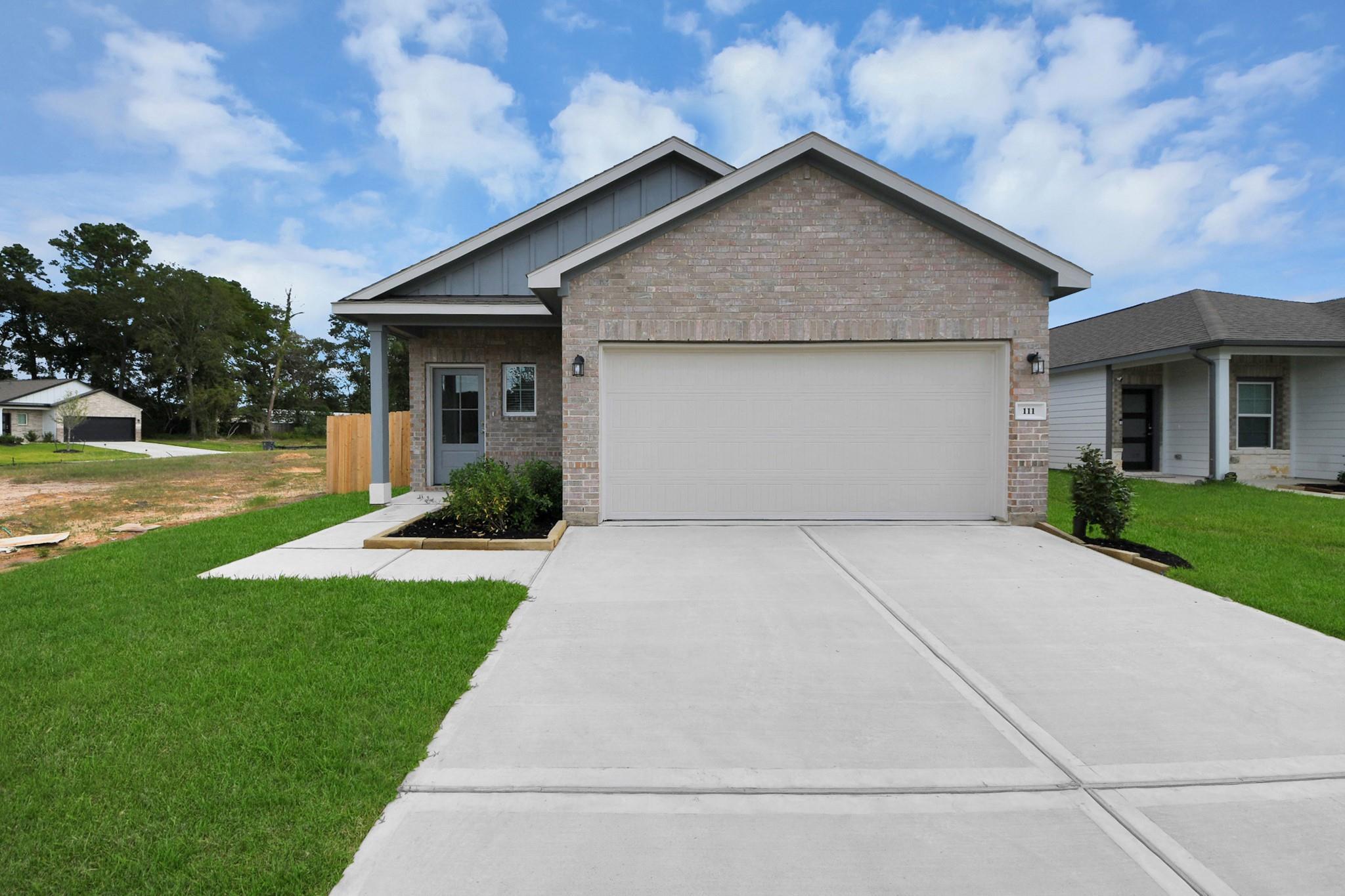 Brick exterior front of Davidson Homes The Sabine F with 2-car garage and landscaped yard in Caney Creek Place, Conroe, Texas