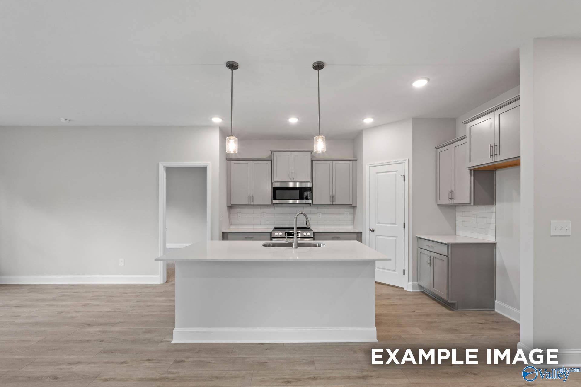 Modern open-concept kitchen with white island, gray cabinets, and pendant lights in The Franklin V, Davidson Homes, Athens, Alabama