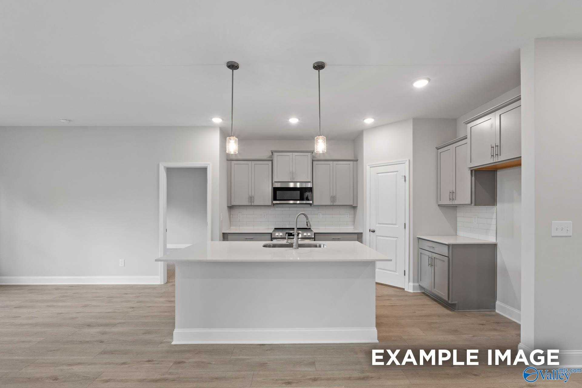 Modern open-concept kitchen with white island, gray cabinets, and pendant lights in The Franklin V, Davidson Homes, Athens, Alabama