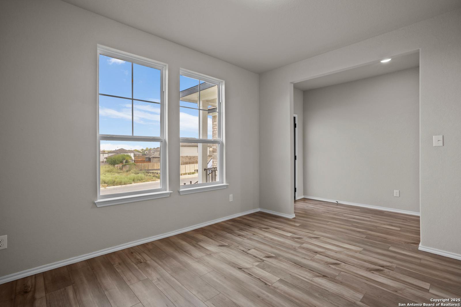 Sunlit empty bedroom with large double windows, blue sky view, neutral walls, hardwood floors in Davidson Homes The Douglas F, San Antonio