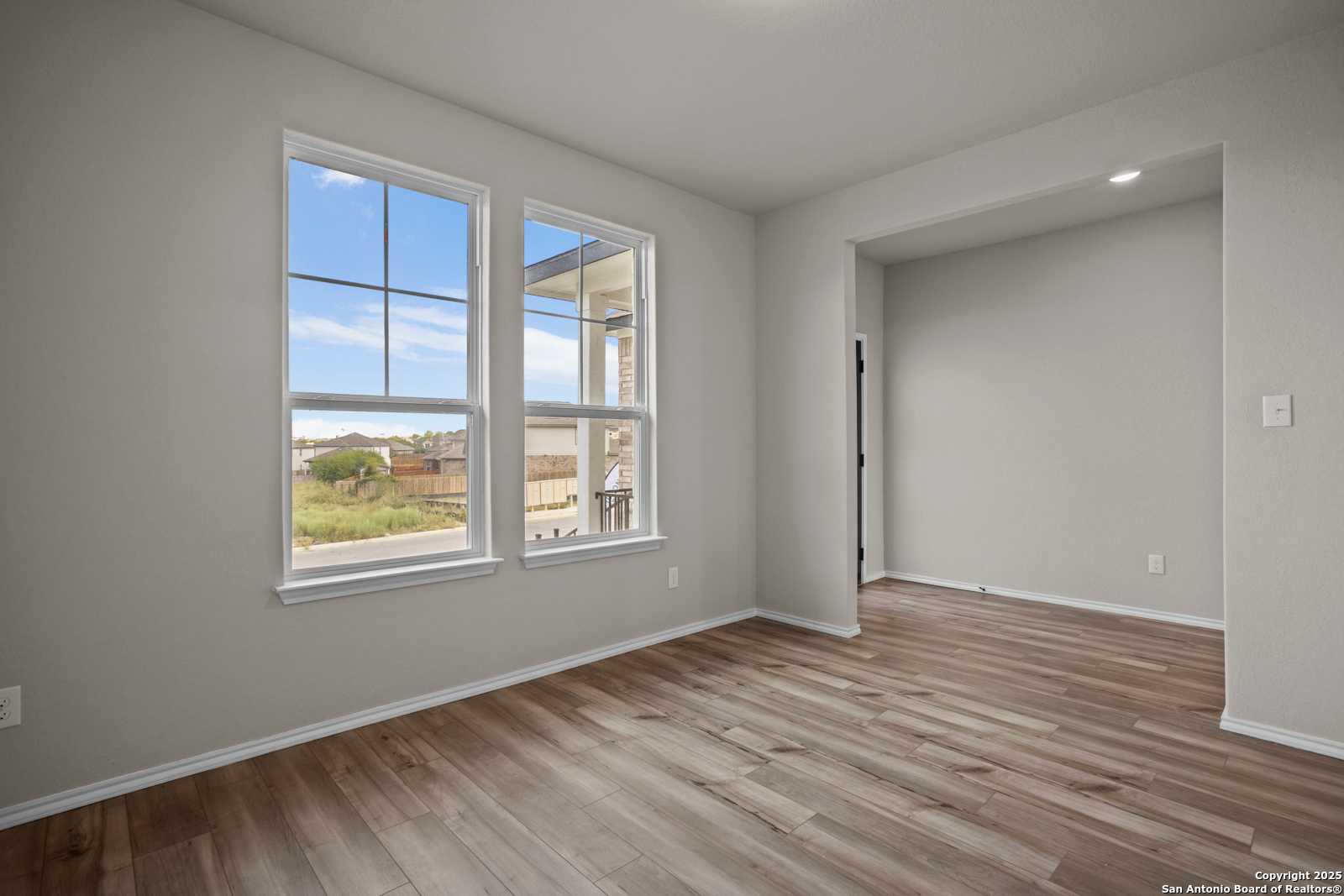 Sunlit empty bedroom with large double windows, blue sky view, neutral walls, hardwood floors in Davidson Homes The Douglas F, San Antonio