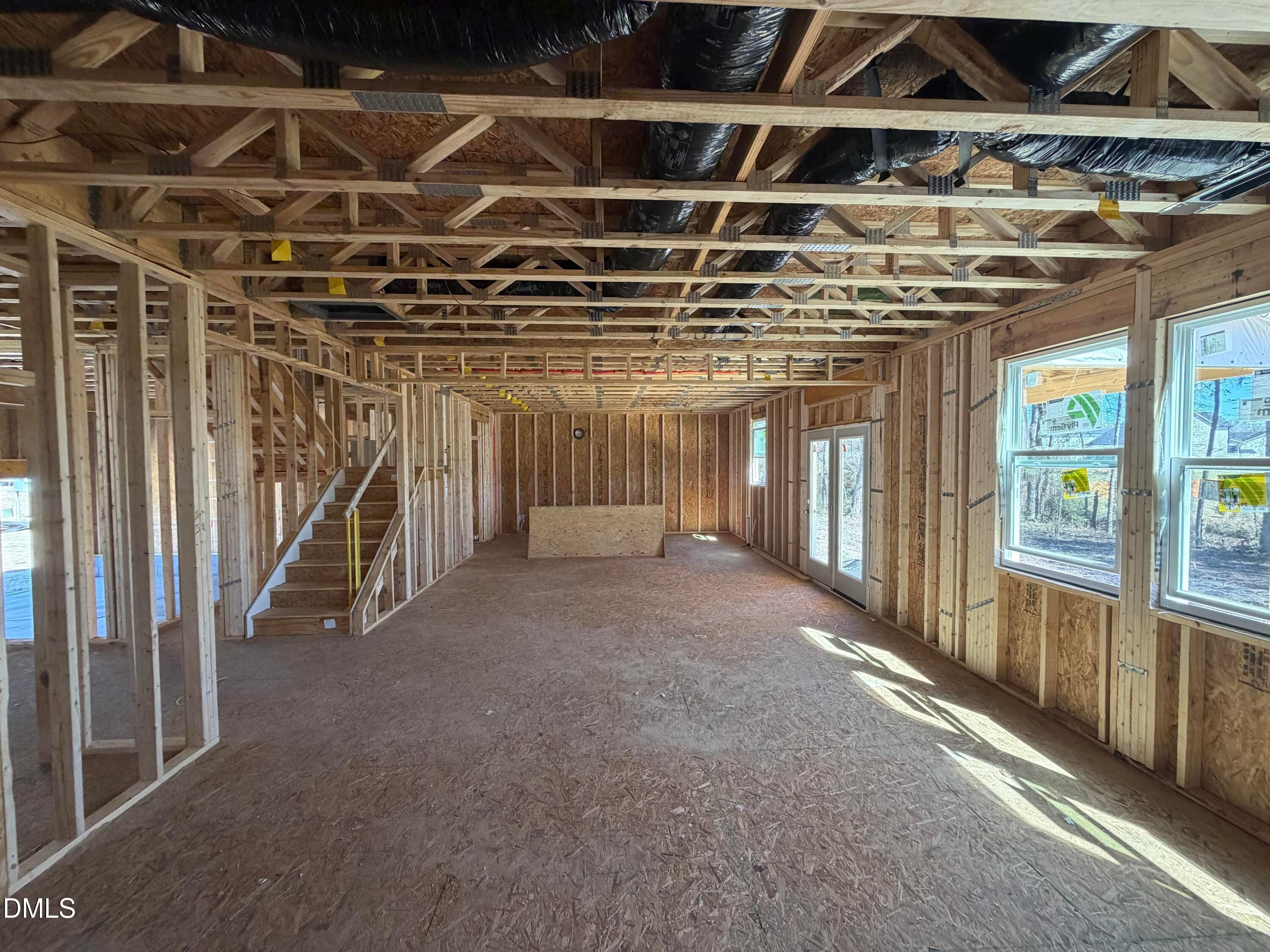 Under construction open living area with wooden framing, exposed ducts, staircase, and large windows in Davidson Homes Hickory II B, Lillington NC