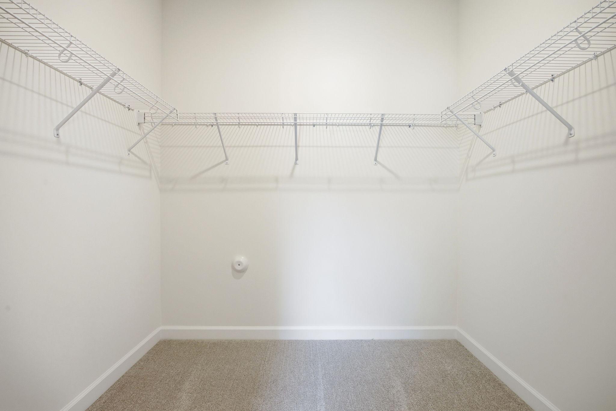Spacious walk-in closet in The Ashport K featuring white wire shelving and plush carpeting.