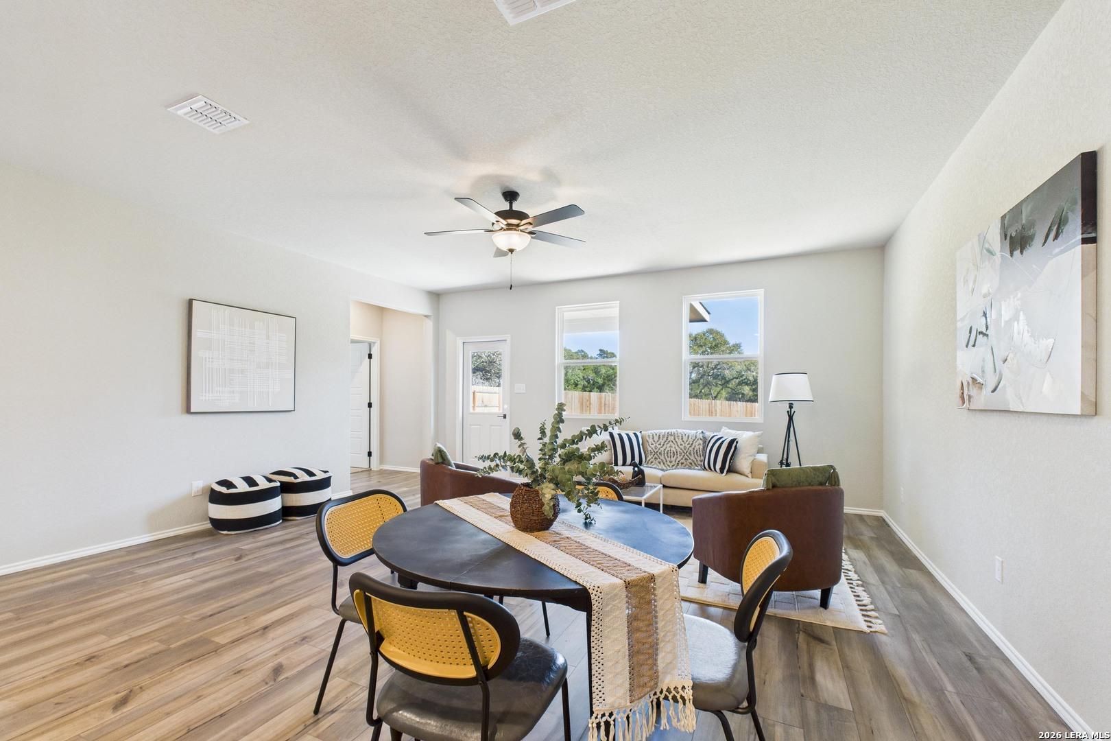 Modern dining area with round wooden table, yellow chairs, beige sofa, and large windows in Davidson Homes The Douglas E, San Antonio