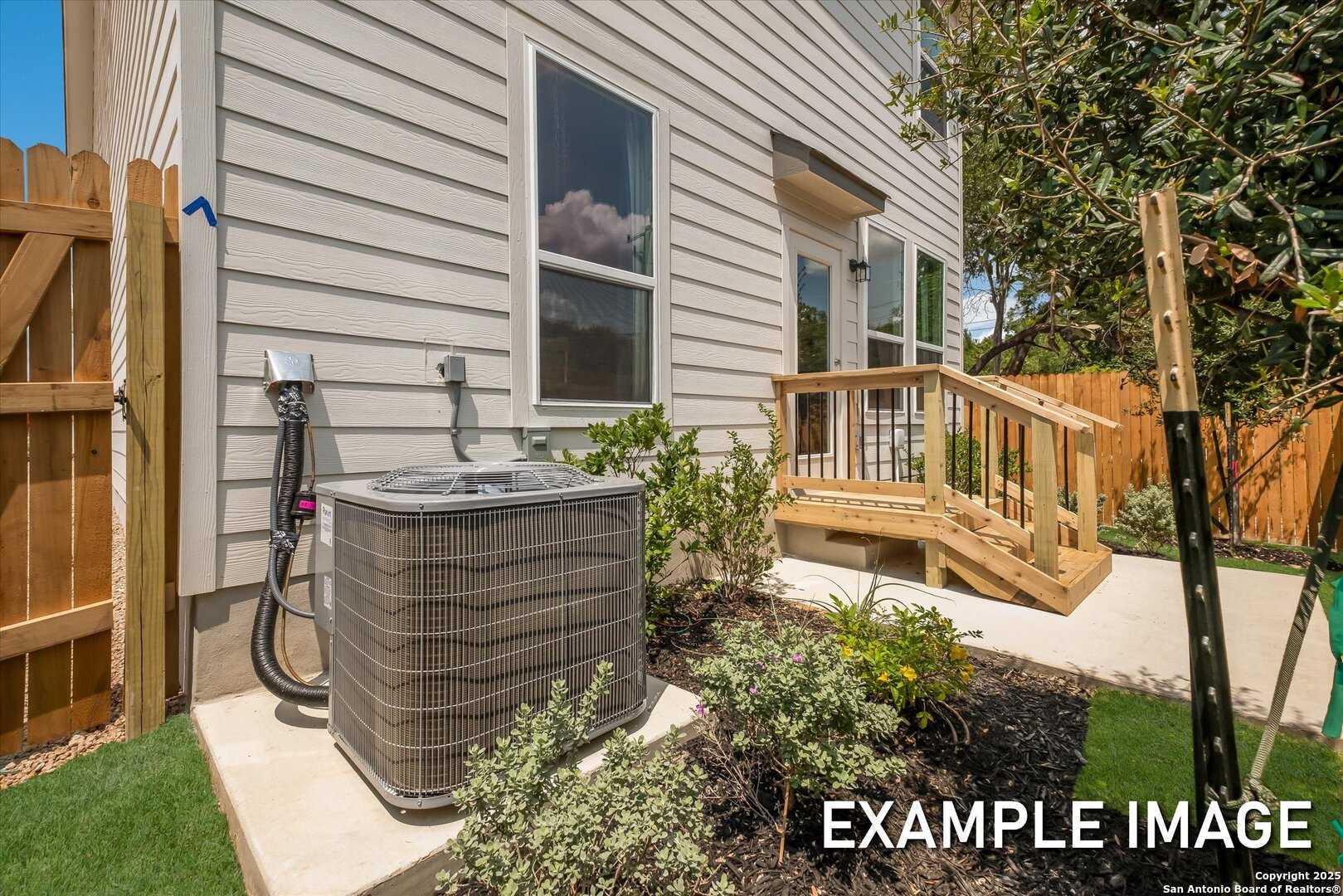 Beige two-story home exterior with wooden deck, AC unit, shrubs, and fenced backyard in Meadows at Oak Creek, San Antonio