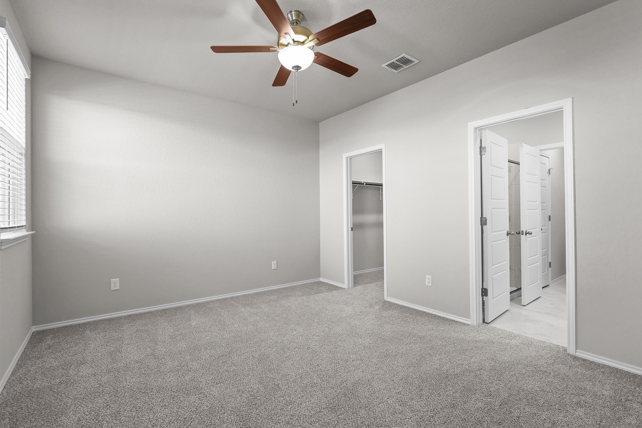 Spacious bedroom in The Colorado B featuring neutral carpet, ceiling fan, walk-in closet, and attached bathroom.