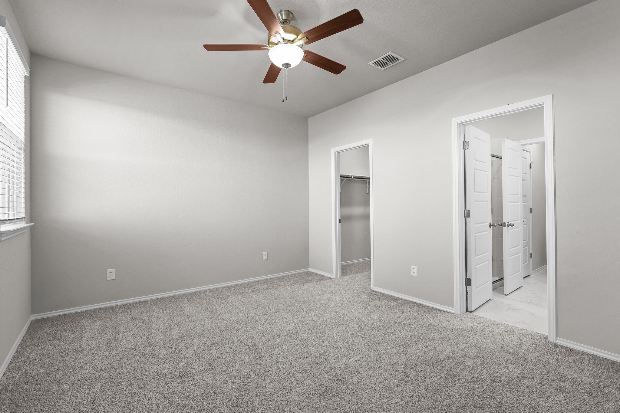 Spacious bedroom in The Colorado B featuring neutral carpet, ceiling fan, walk-in closet, and attached bathroom.
