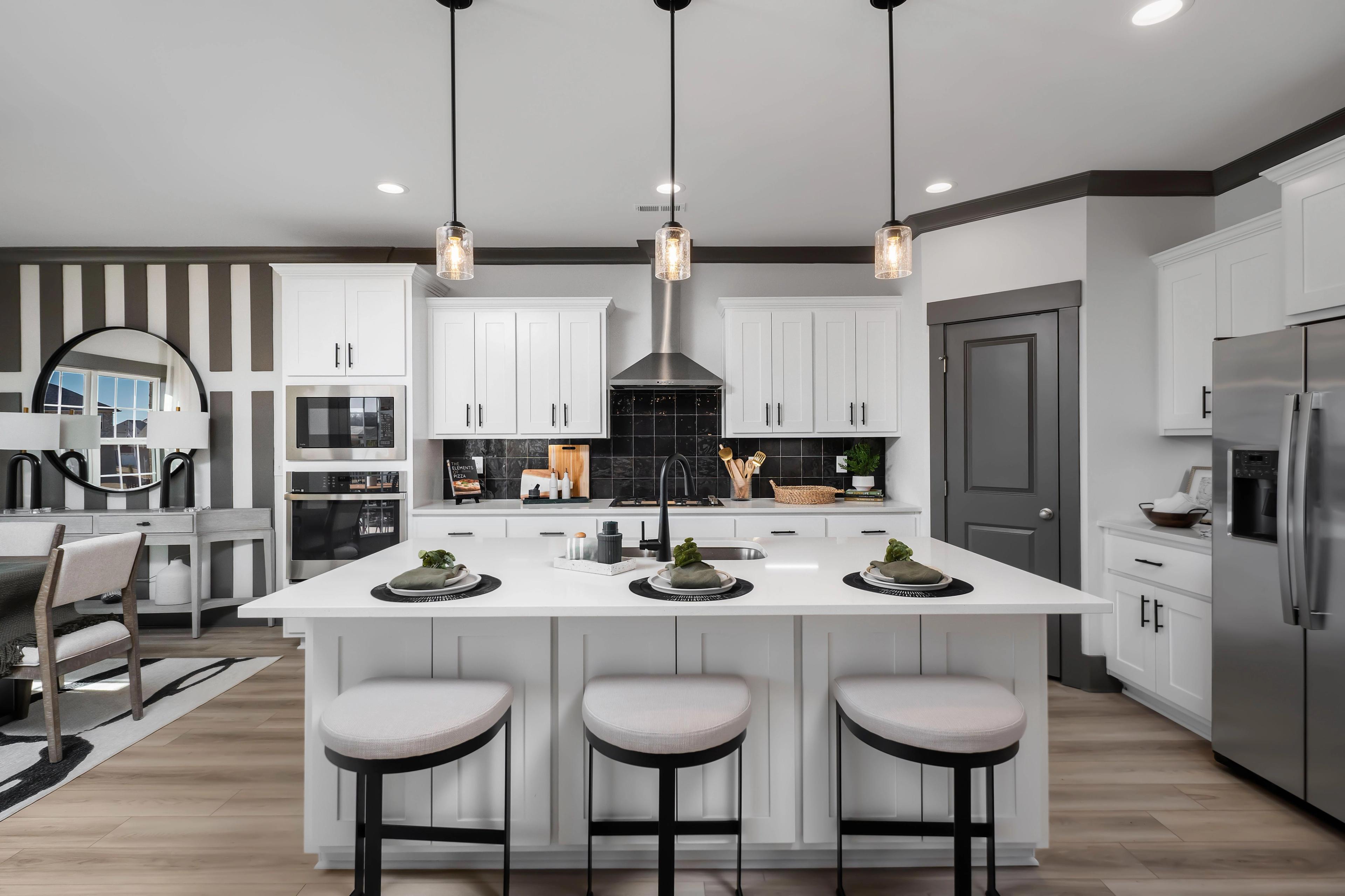 Spacious white kitchen in Barnett's Crossing home, Madison Alabama, with central island, bar stools, stainless appliances, and black accents