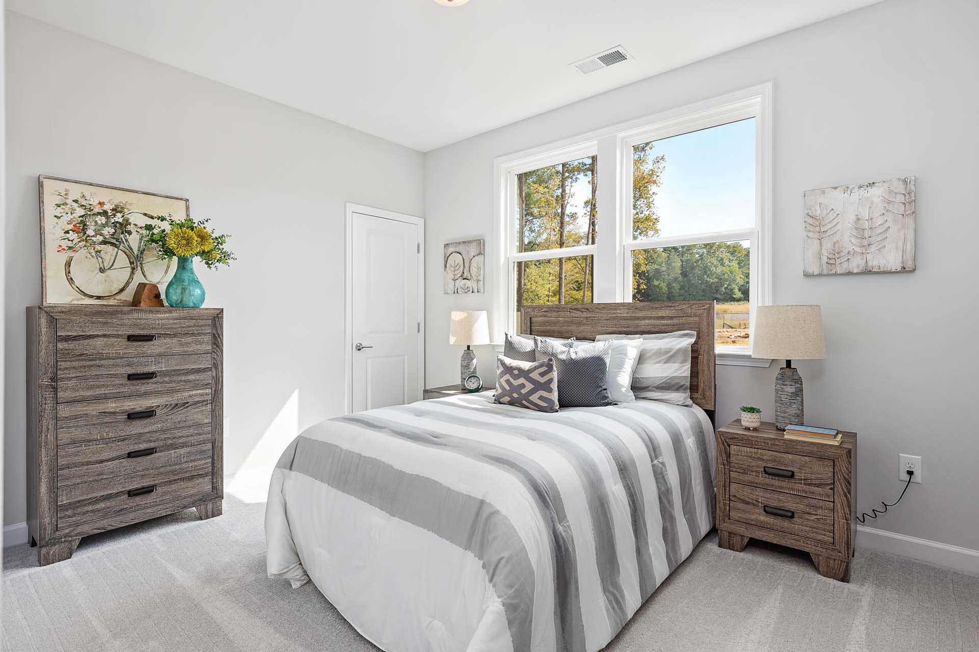 Spacious gray bedroom at Prince Place in Fuquay-Varina NC with striped bedding, wooden dresser, and large sunny windows