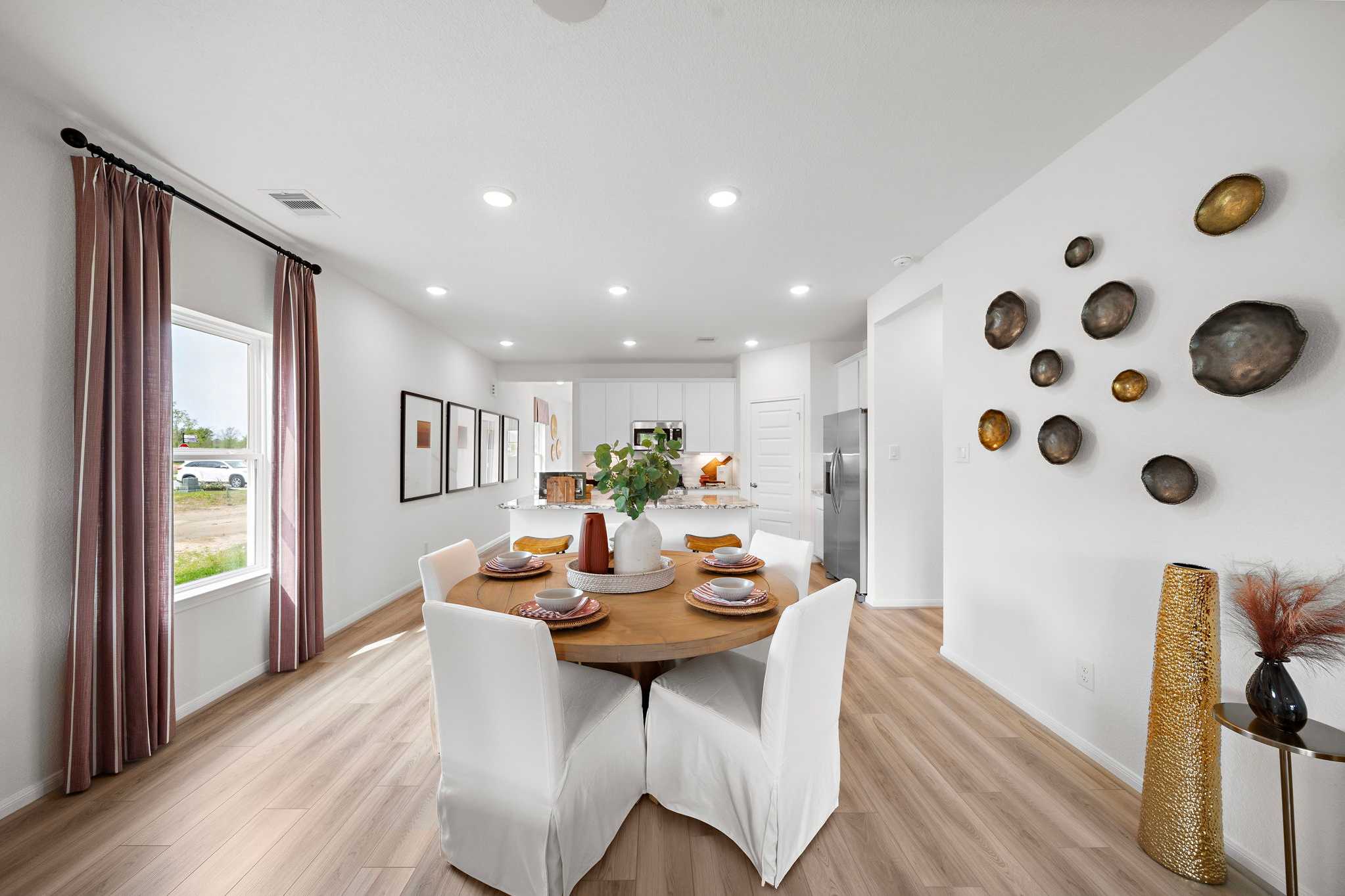 Open-concept dining area at The Villages at WestPointe in Dayton Texas with round wooden table, white chairs, and modern kitchen