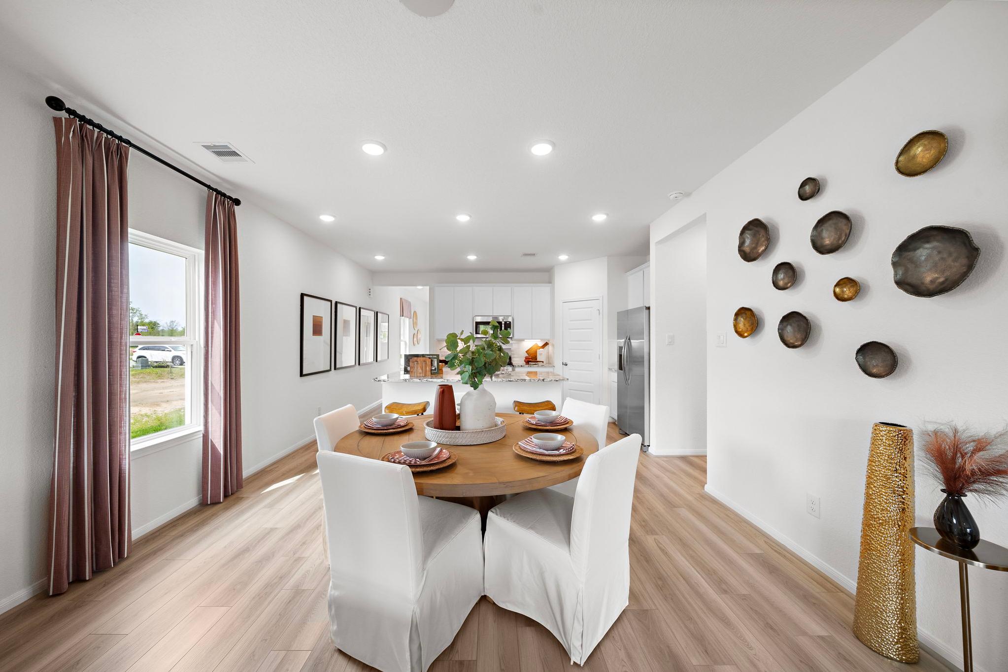Open-concept dining area at The Villages at WestPointe in Dayton Texas with round wooden table, white chairs, and modern kitchen