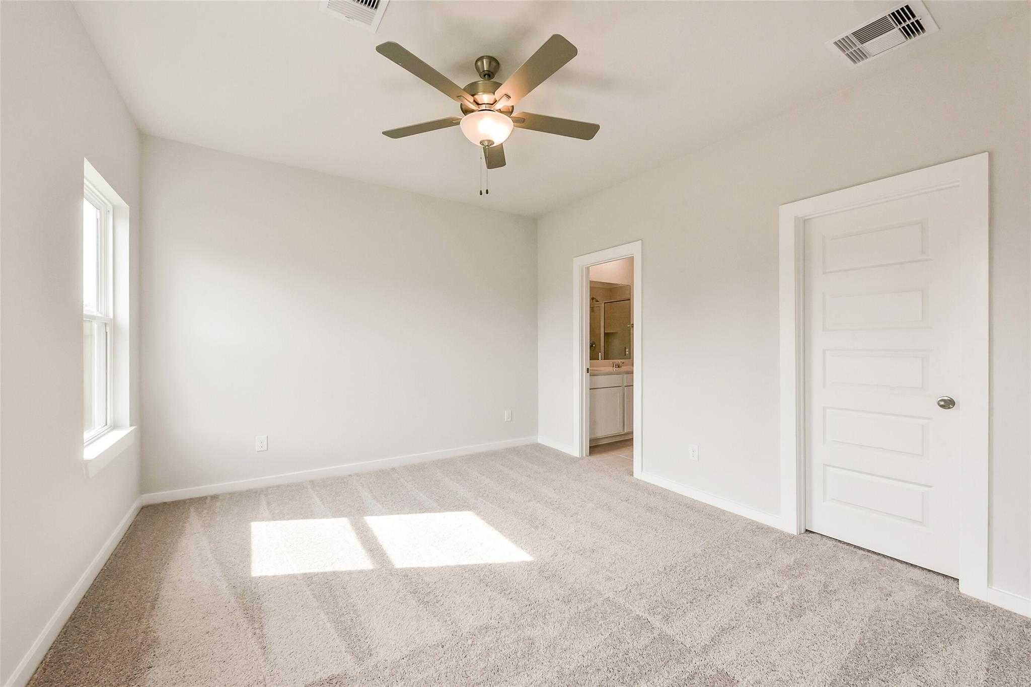 Bright carpeted bedroom with ceiling fan, windows, and en-suite bath in Davidson Homes The Comal G, Dayton, Texas