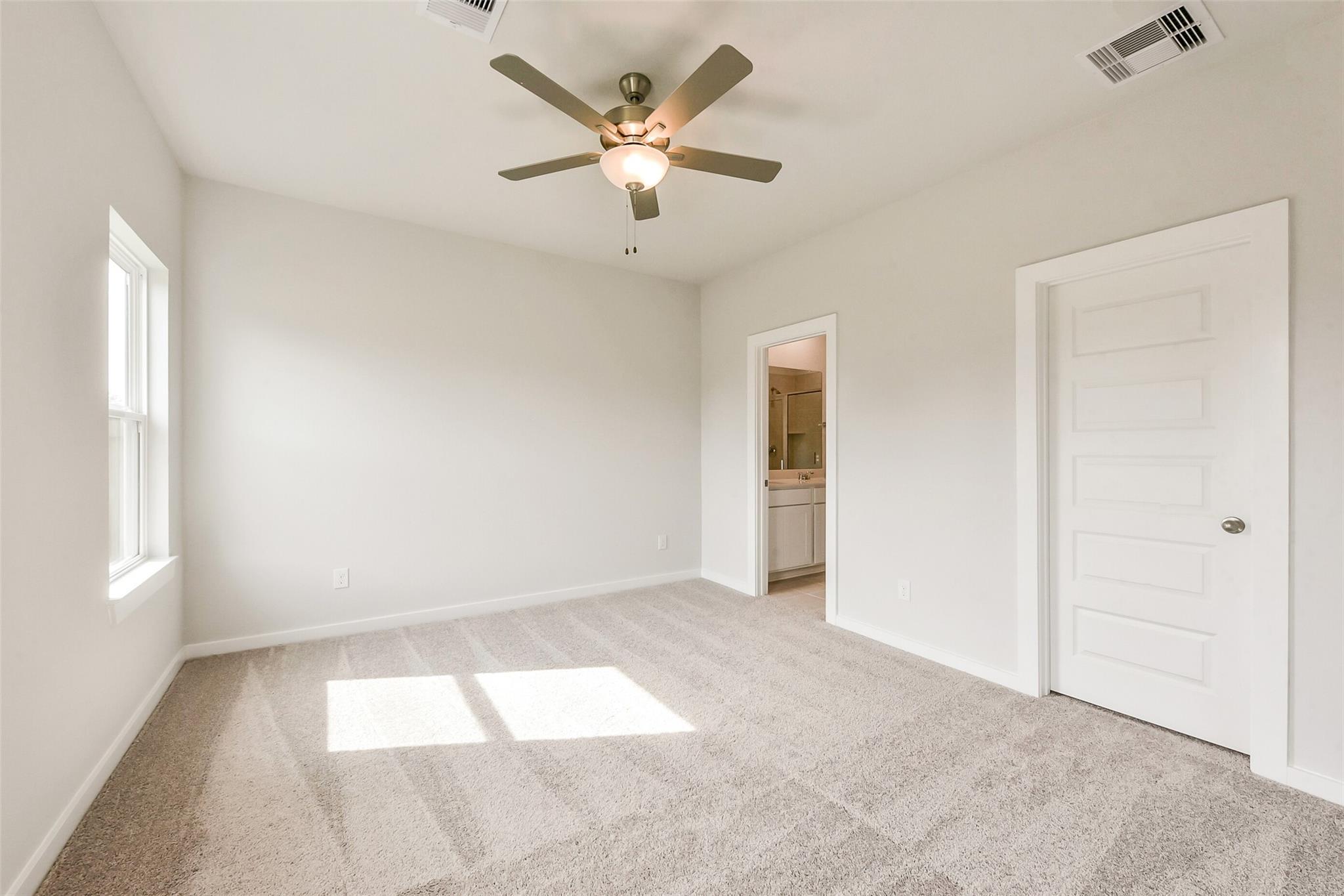 Bright bedroom featuring ceiling fan, carpet flooring, and adjacent bathroom in Davidson Homes The Comal G, Dayton, Texas