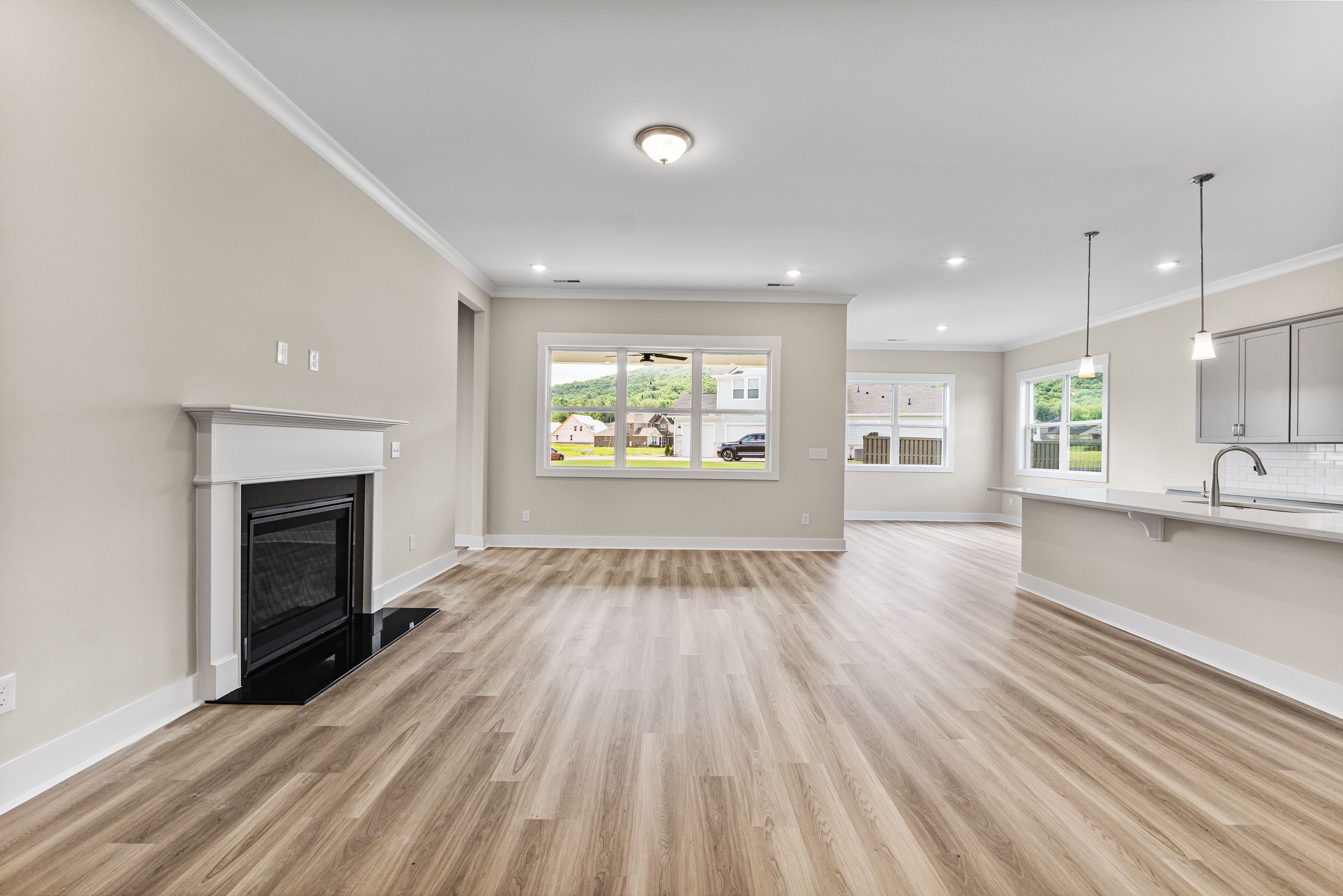 Spacious open living room in The Oxford A with gas fireplace, hardwood floors, and adjacent white kitchen island