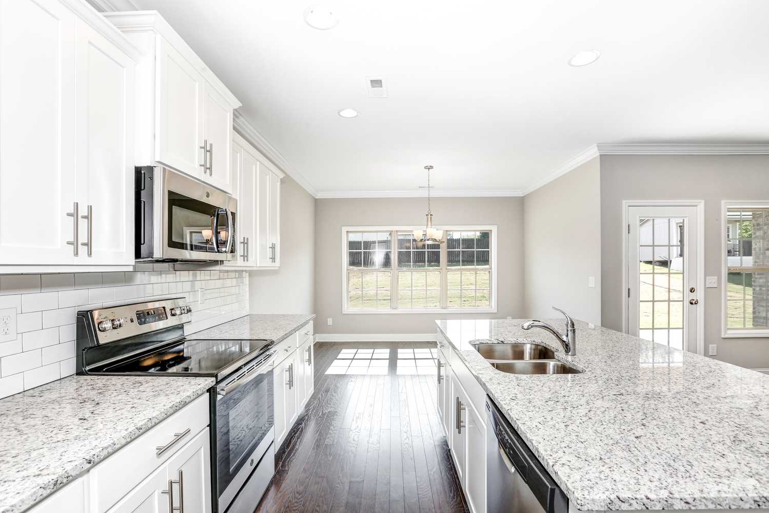Spacious kitchen in The Montgomery home featuring white cabinets, granite counters, stainless appliances, and adjacent dining area