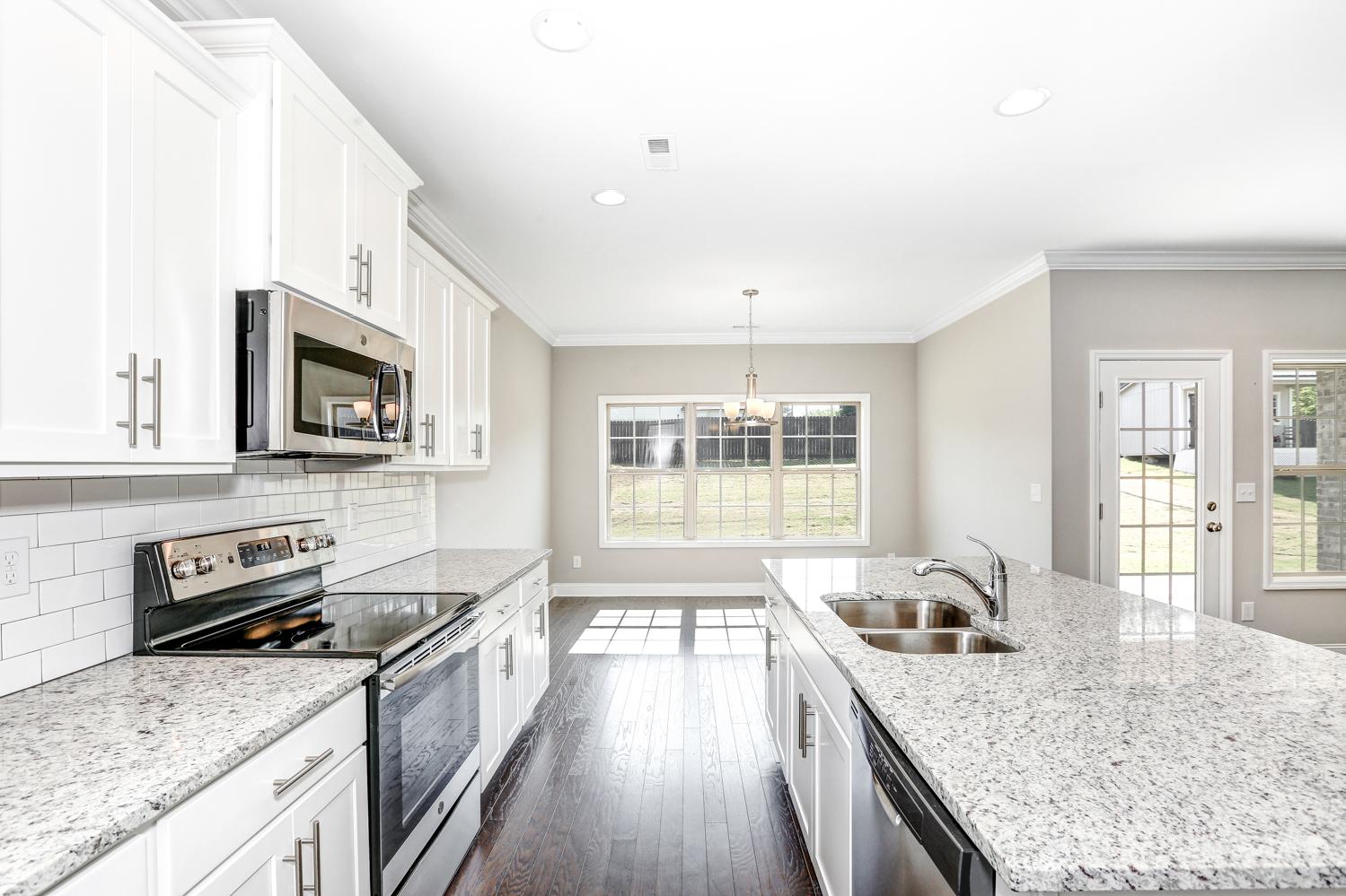 Spacious kitchen in The Montgomery home featuring white cabinets, granite counters, stainless appliances, and adjacent dining area