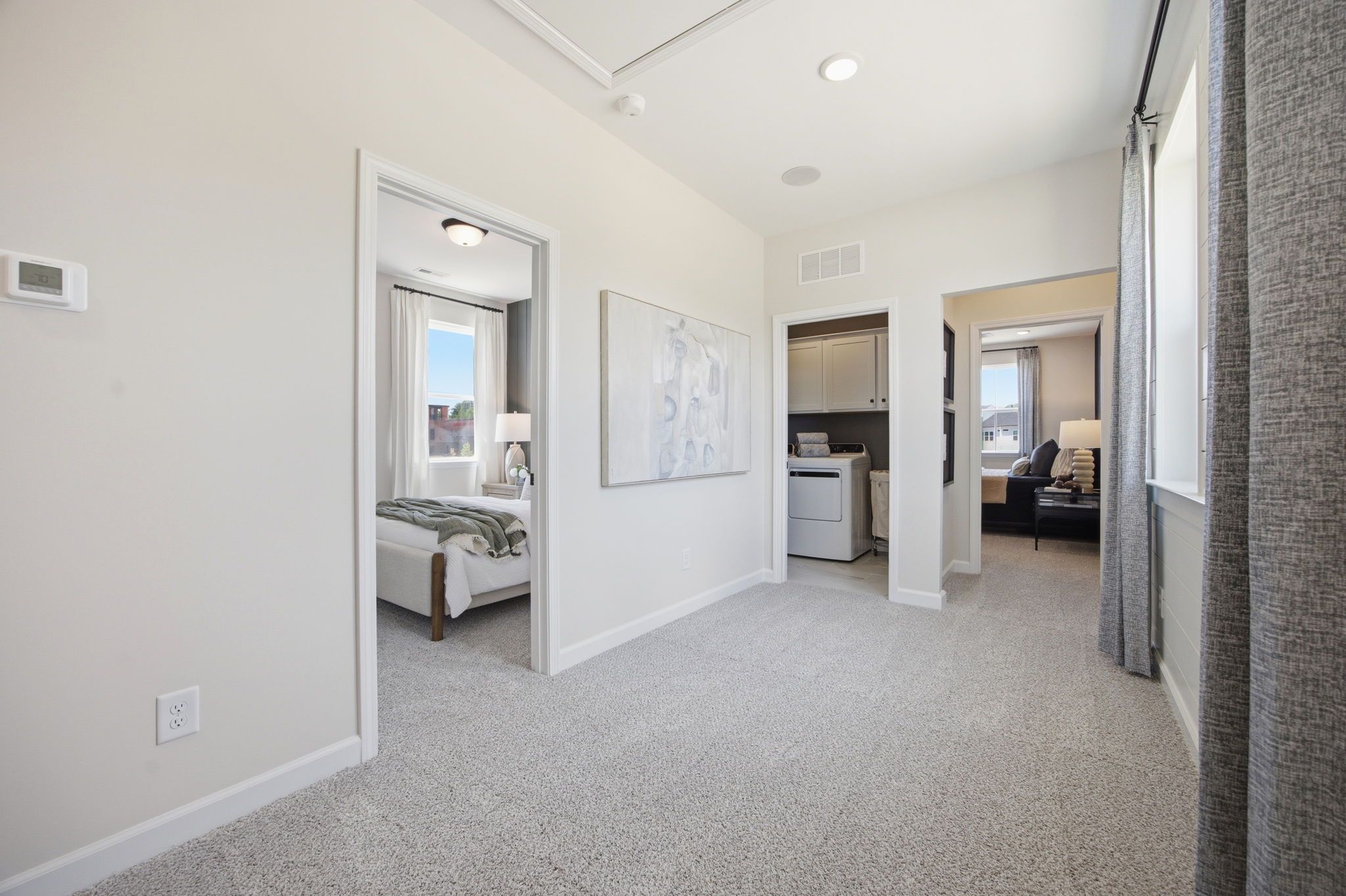 Spacious upstairs hallway in Forestville Yard Knightdale NC home featuring beige walls, gray carpet, bedrooms, and laundry room