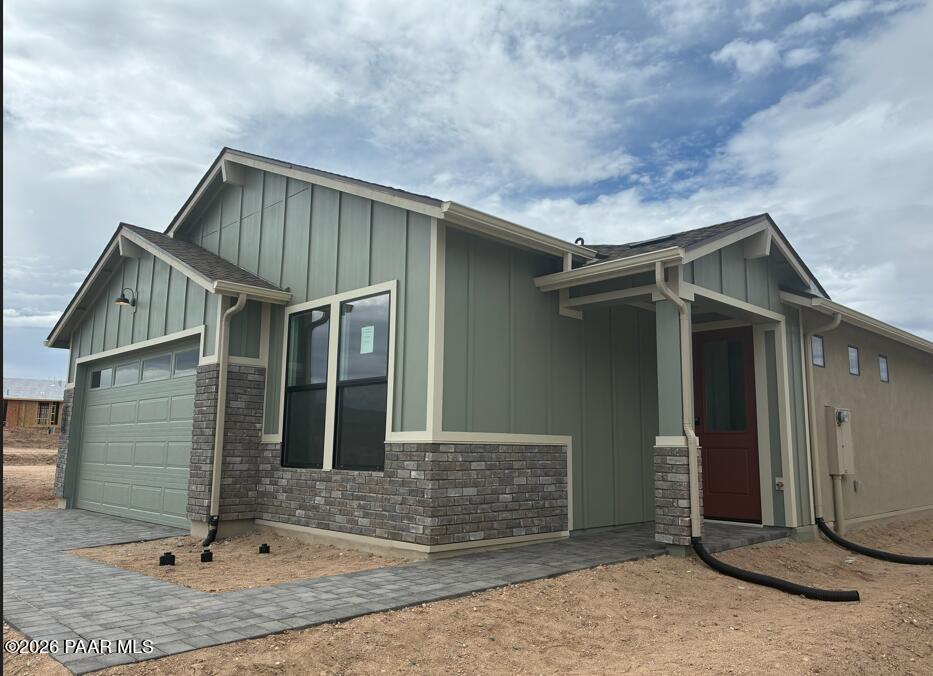 Modern single-story home with sage green siding, brick accents, 2-car garage, red entry door in South Ranch, Prescott AZ
