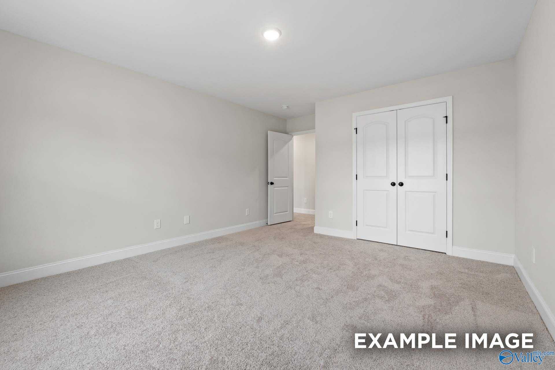 Spacious empty master bedroom with walk-in closet doors, beige carpet, and neutral walls in Davidson Homes The Camden D, Huntsville