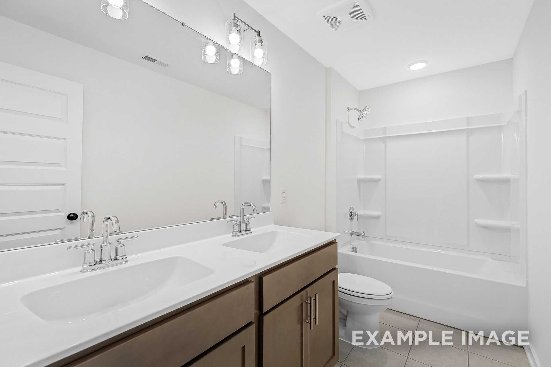 The Logan B master bathroom featuring double sink vanity, soaking tub, toilet, and modern white finishes by Davidson Homes