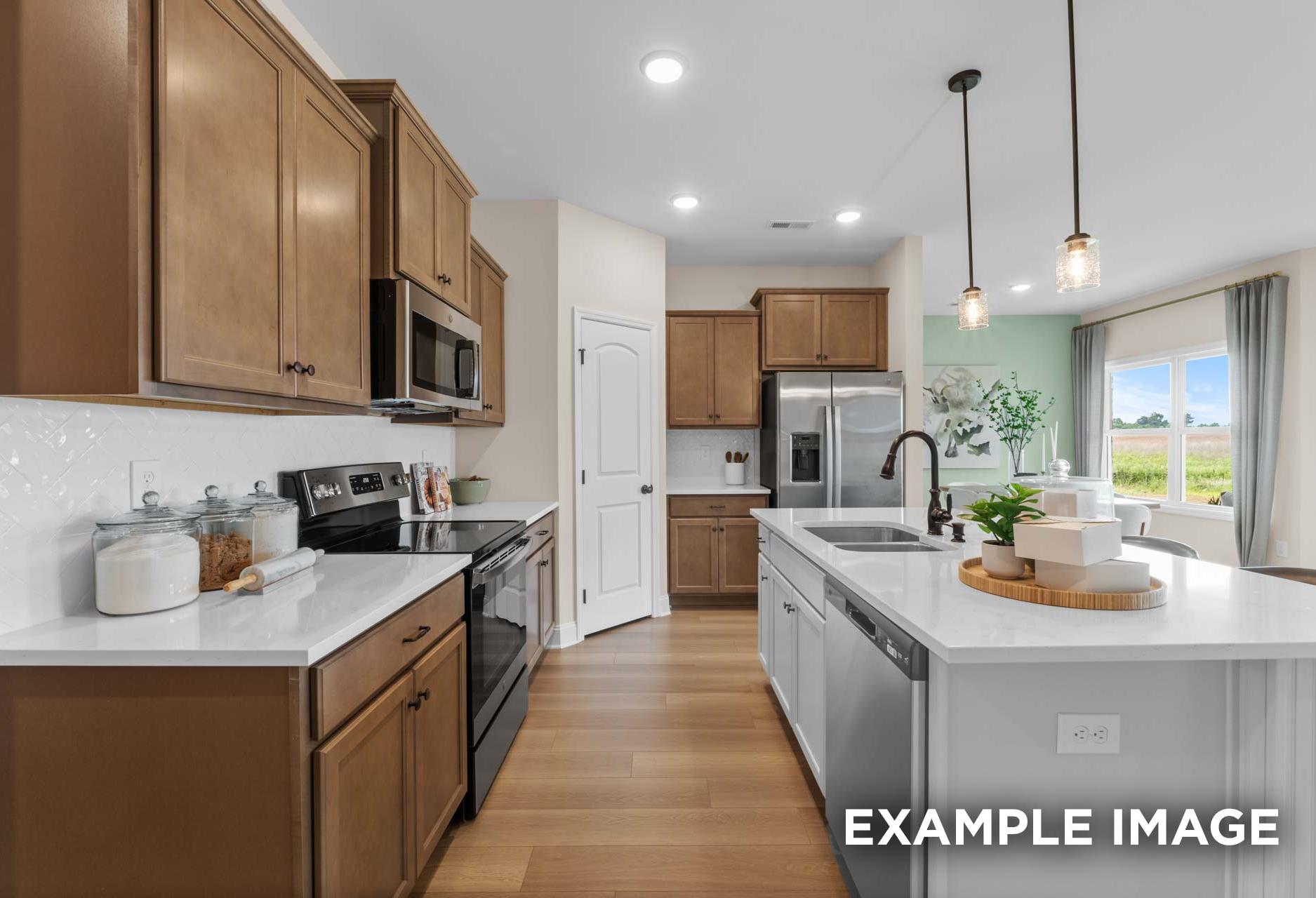 The Laurel M kitchen featuring warm shaker cabinets, white quartz island with sink, stainless steel appliances, and pendant lights
