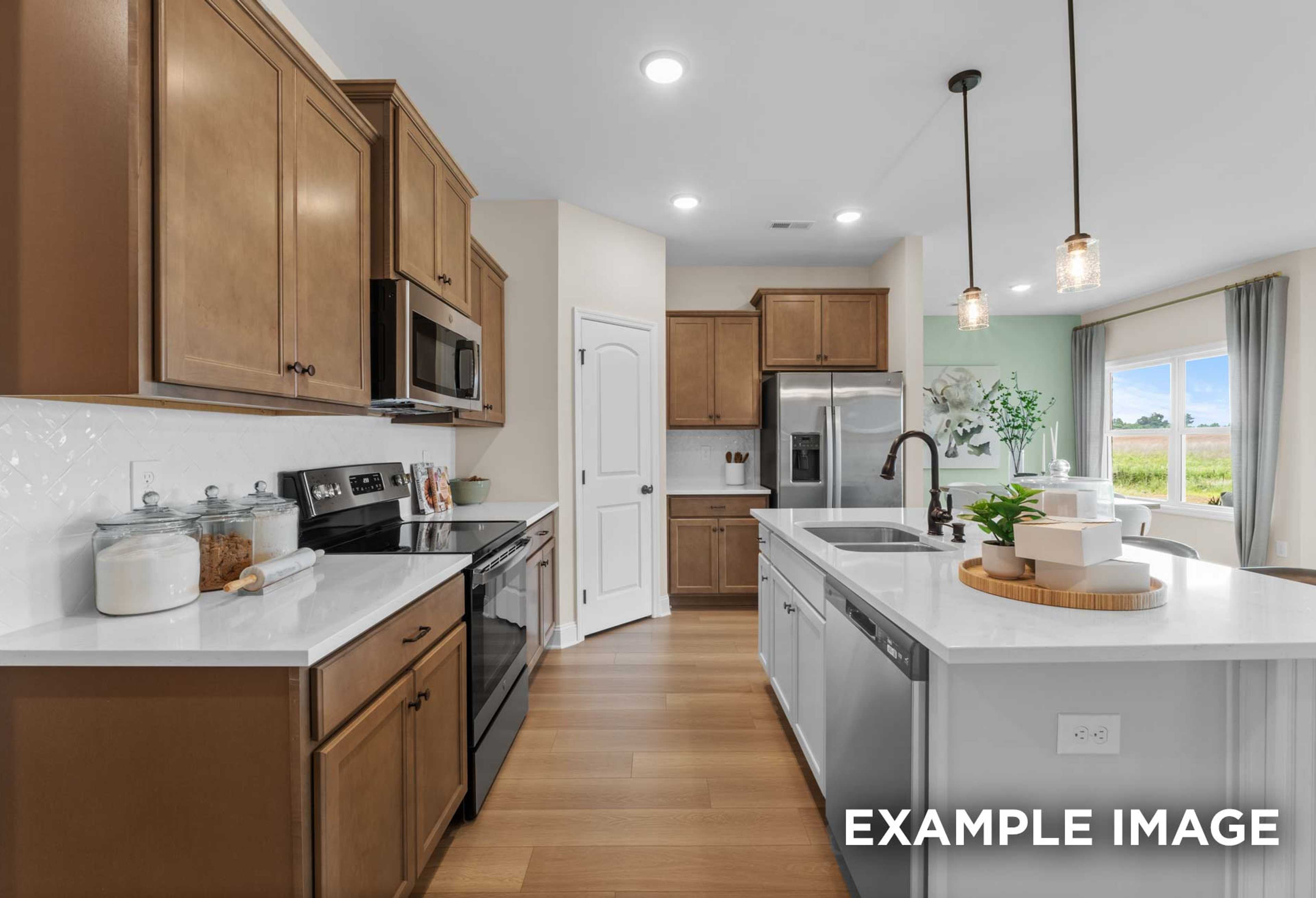 The Laurel M kitchen featuring warm shaker cabinets, white quartz island with sink, stainless steel appliances, and pendant lights