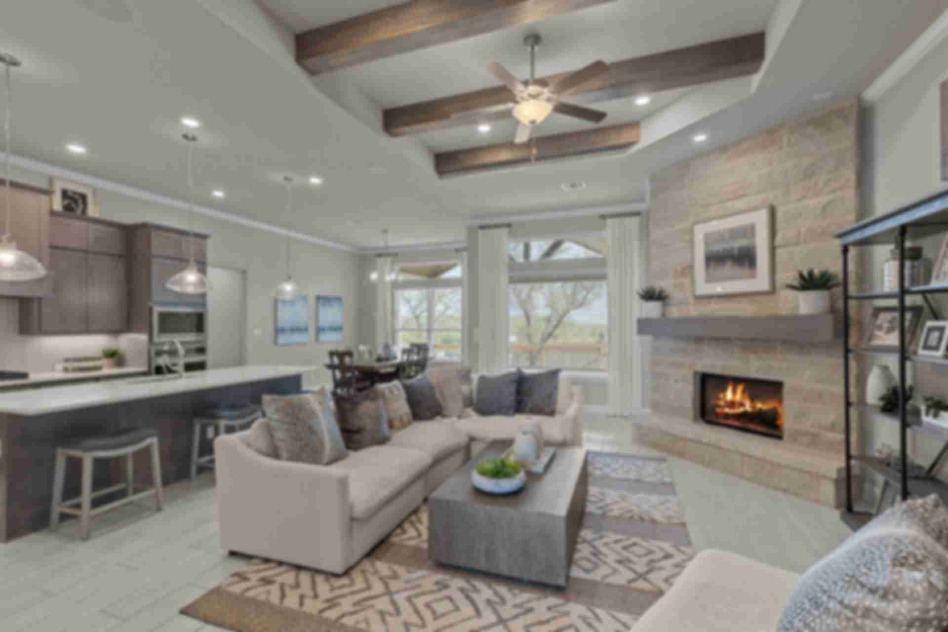 Spacious open-concept living room and kitchen at The Reserve at Potranco Oaks in Castroville Texas with stone fireplace, vaulted beams