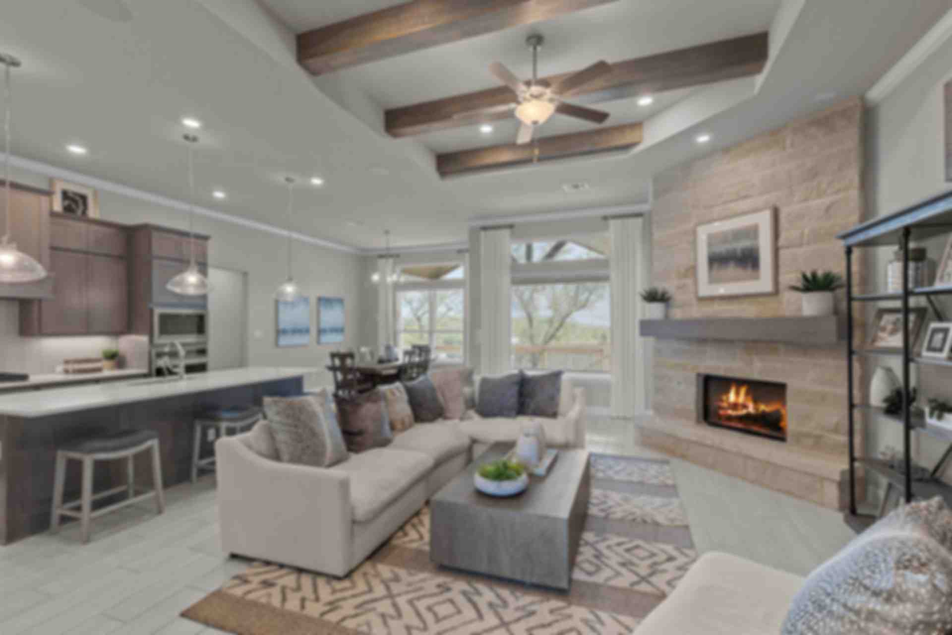 Spacious open-concept living room and kitchen at The Reserve at Potranco Oaks in Castroville Texas with stone fireplace, vaulted beams
