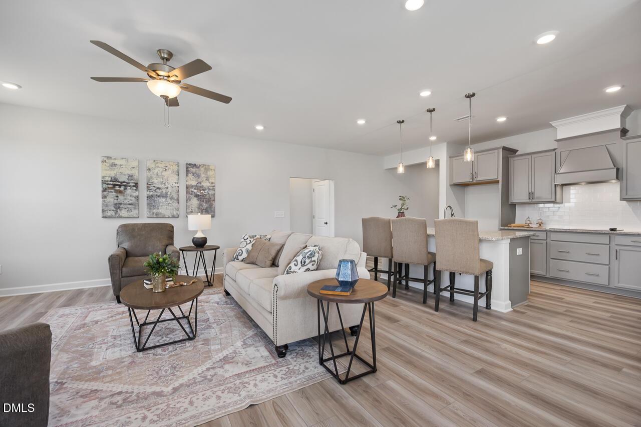 Open-concept living room with beige sofa, coffee table, and rug flowing into gray cabinet kitchen island in The Daphne D by Davidson Homes, Lillington, NC